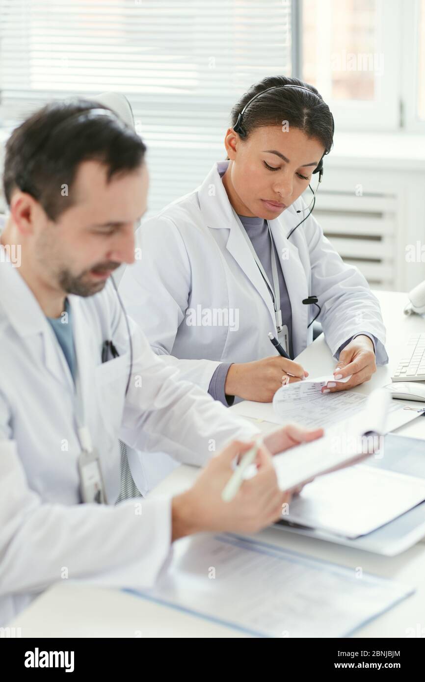 Zwei seriöse Ärzte sitzen am Tisch und erledigen gemeinsam im Büro Schreibarbeit Stockfoto