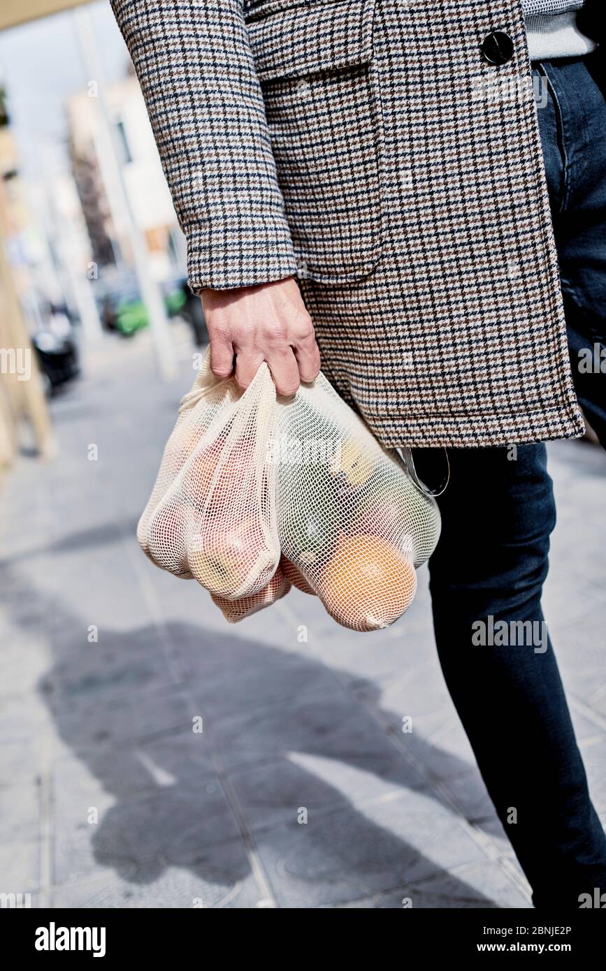 Nahaufnahme eines Mannes auf der Straße, der einen wiederverwendbaren Textil-Netzbeutel trägt, der früher Lebensmittel in großen Mengen, voller Obst und Gemüse, als Maßnahme zum Redu kaufte Stockfoto