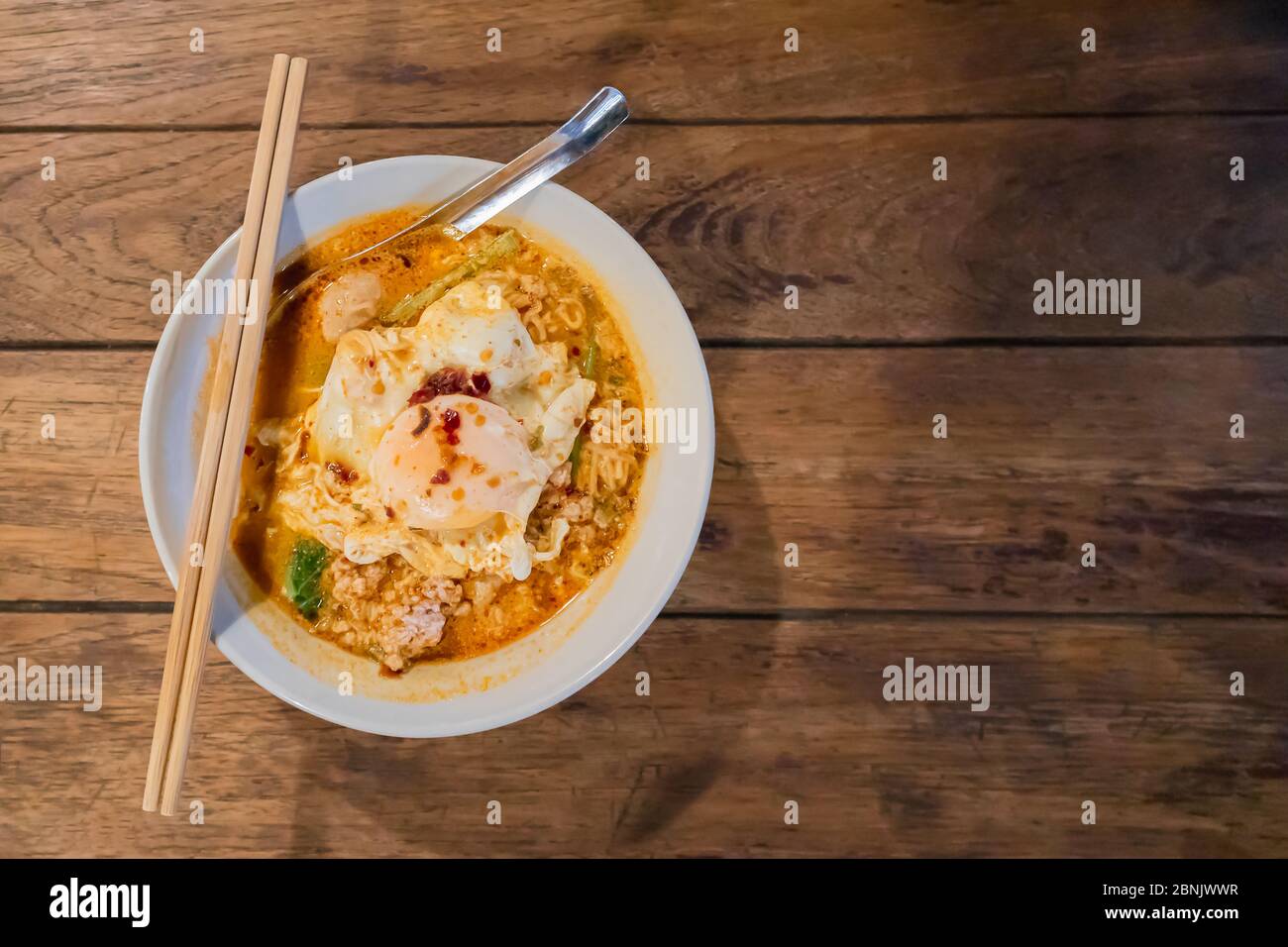 Draufsicht auf Tom Yum Nudeln mit gehacktem Schweinefleisch und Spiegelei auf Holztisch Stockfoto