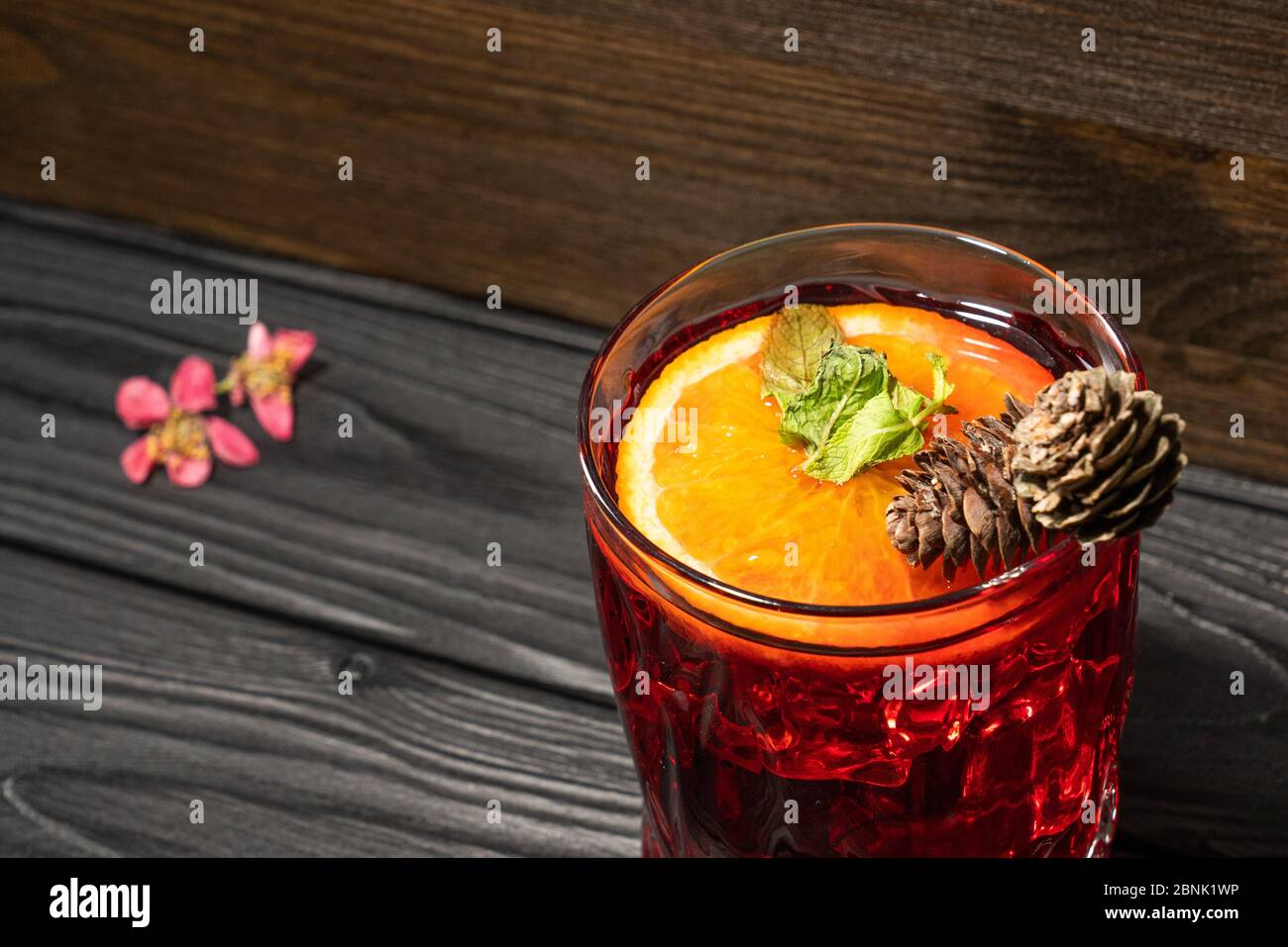 Frischer Cocktail mit Orange, Minze und Eis, verziert mit Zapfen auf einem Holztisch mit rosa Blumen Stockfoto