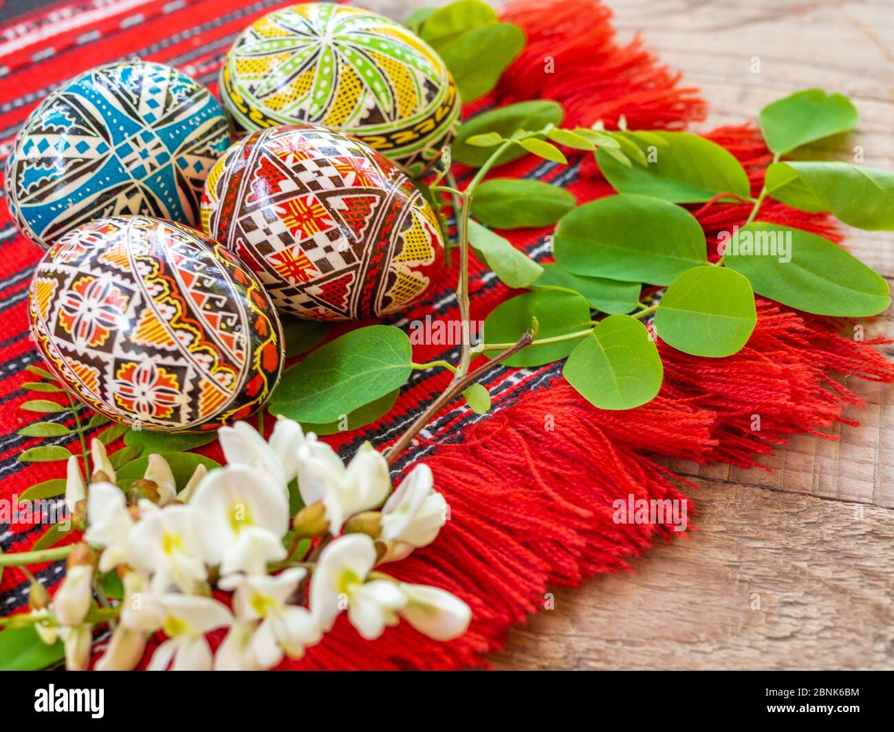 Schön handverzierte rumänische orthodoxe ostereier mit traditionellen Motiven auf einem roten Tuch mit Akazienblumen beiseite Stockfoto