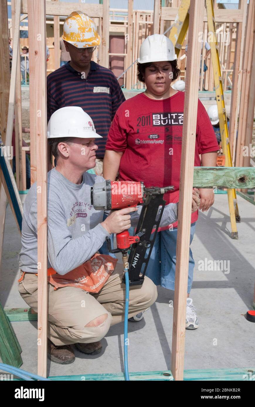 Der Freiwillige ist ein Hengst, wie andere Freiwillige beim Bau eines erschwinglichen Hauses mit Habitat for Humanity zusehen. Habitat für die Menschheit finanziert und baut ein Haus, das sich Einwohner mit niedrigem Einkommen durch zinslose Hypotheken leisten könnten. ©Bob Daemmrich Stockfoto