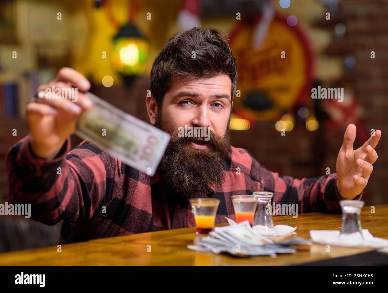 Hipster hält Geld, Bargeld, um mehr Alkohol zu kaufen. Mann mit betrunkenem Gesicht sitzen alleine an der Theke. Guy verbringen Freizeit in Bar trinken Cocktail, defokussed Hintergrund. Get Drunk Concept. Stockfoto