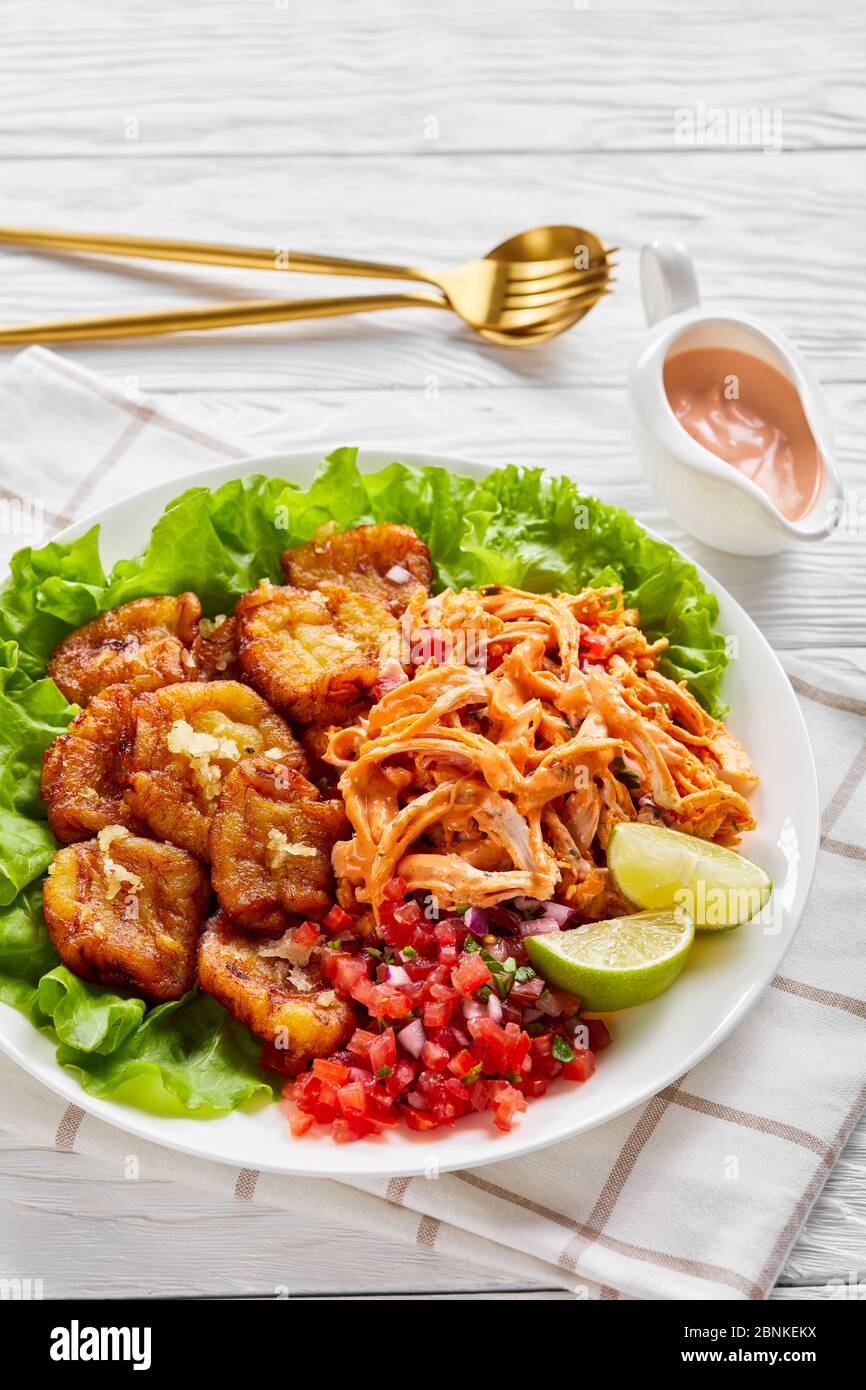 Geschreddertes Huhn mit Büffelsauce, Pico de gallo Salsa, Limettenkeile mit gebratenen Kochbananen auf frischen Salatblättern serviert, auf einem weißen Teller auf einem Stockfoto