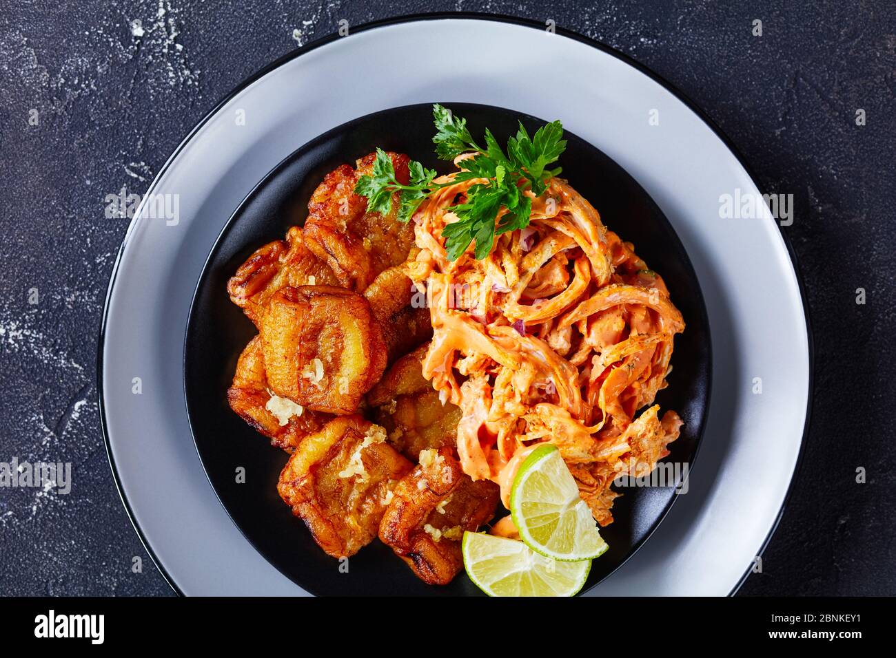 Zweimal gebratene Kochbananen karibisches Fingerfood mit geschreddertem Huhn mit Ketchup und Mayonnaise-Sauce auf schwarzem Teller, Draufsicht, Nahaufnahme Stockfoto