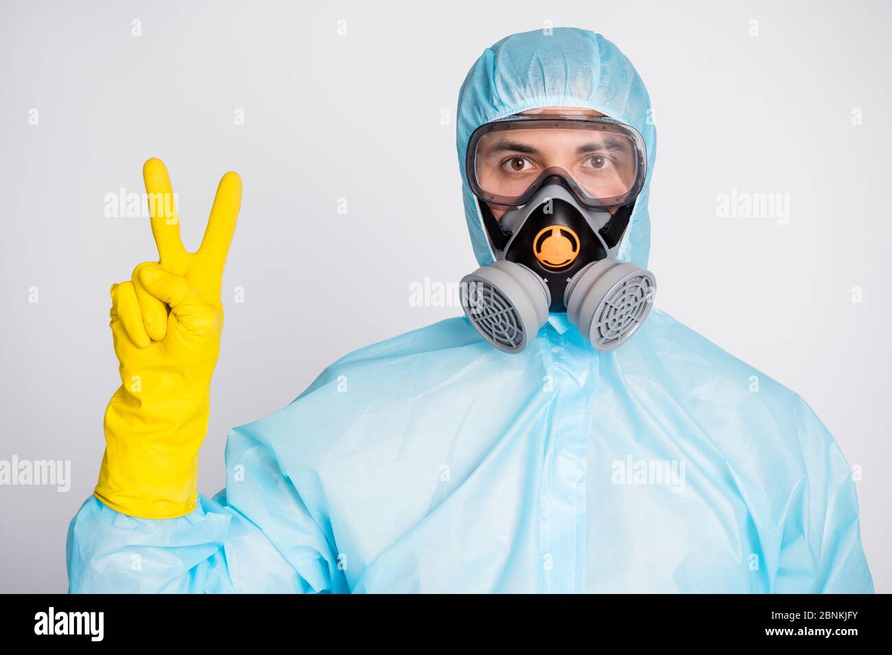 Porträt von medizinischen Arbeiter Mann in weißen hazmat einheitliche Atemmaske machen V-Zeichen isoliert über grauen Hintergrund Stockfoto