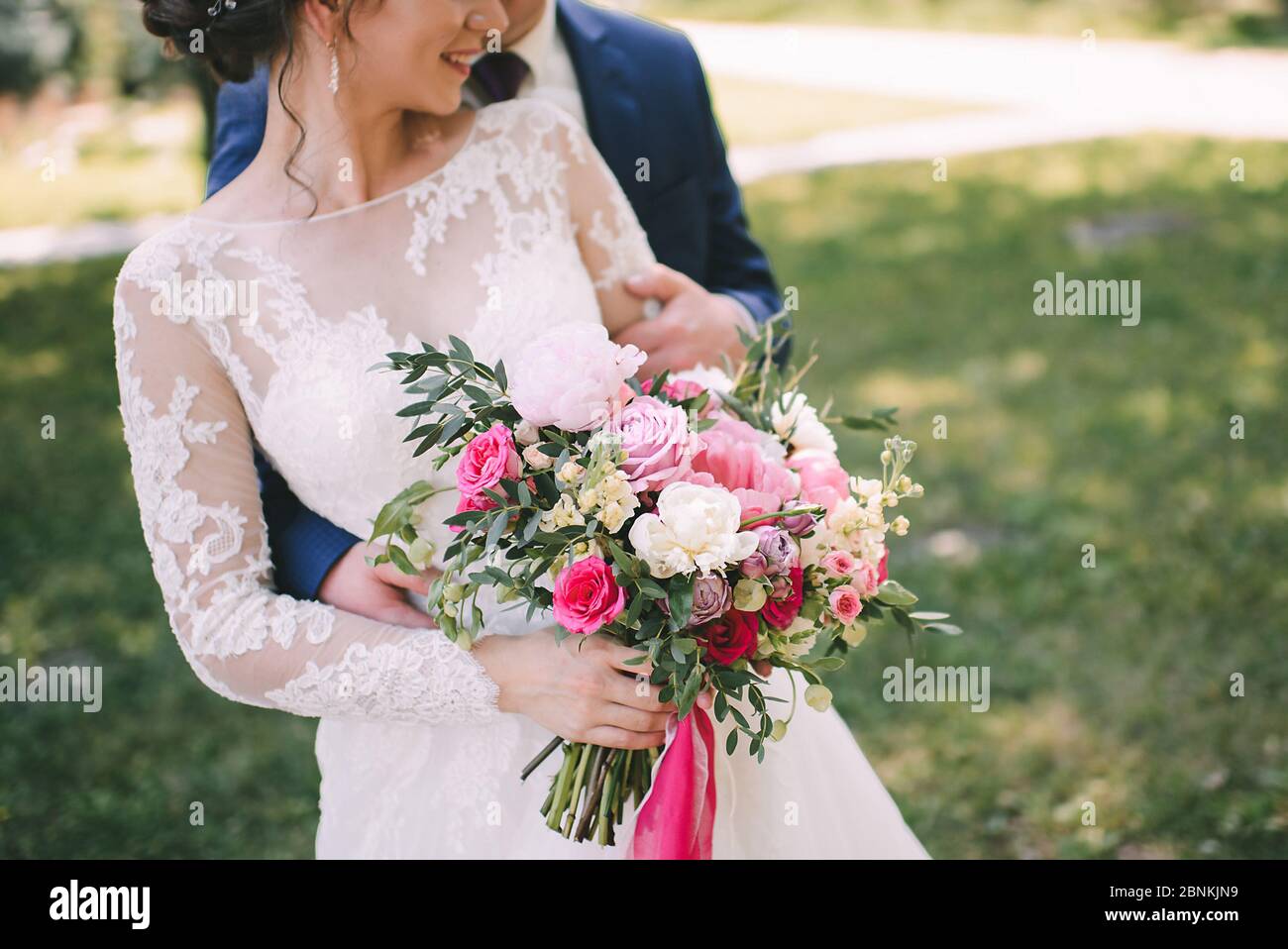 Nahaufnahme des Bouquets einer Braut aus Pfingstrosen, Rosen, Eukalyptus in weiß-rosa Schattierungen, die mit rosa Bändern gebunden sind. Die Braut hält einen Strauß in der Hand in einem Wh Stockfoto