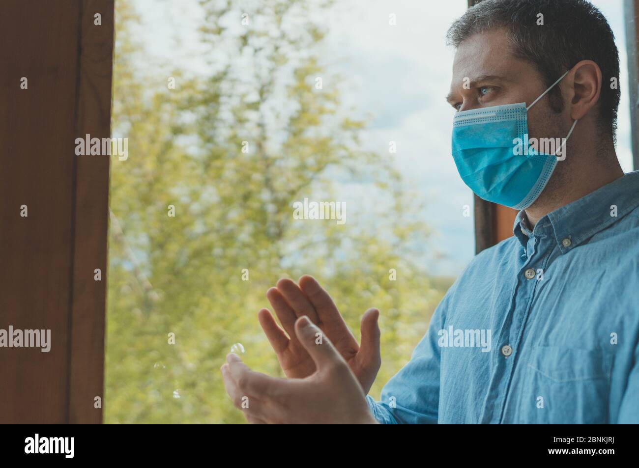 Mann in medizinischer Maske steht auf dem Balkon und applaudiert den Sanitätern. Bleib zu Hause. Stockfoto