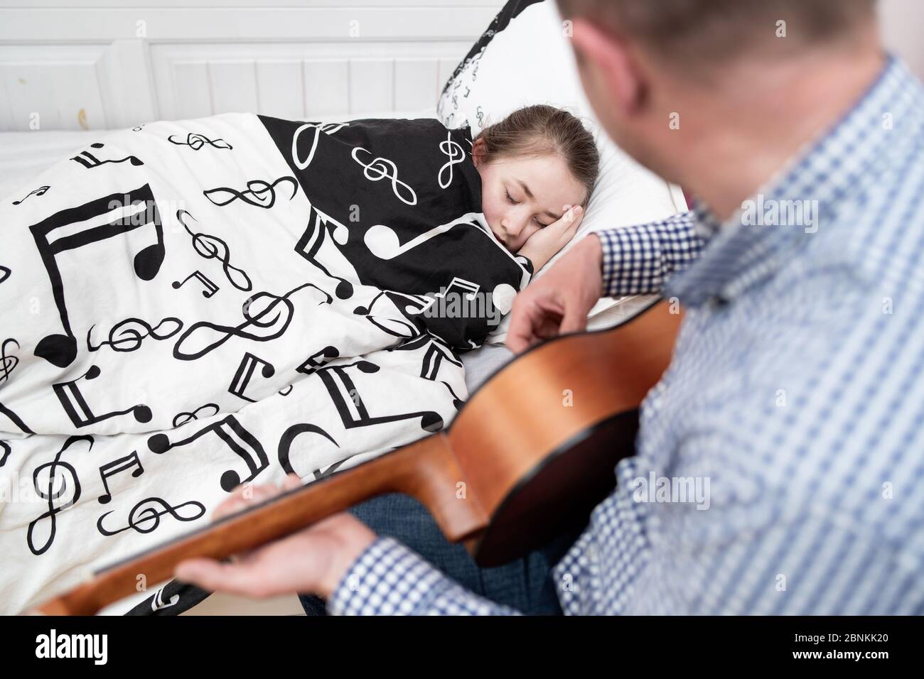 Vater spielt Gitarre für Tochter mit Grippe. Väterliche Liebe. Kinderbetreuung. Stockfoto