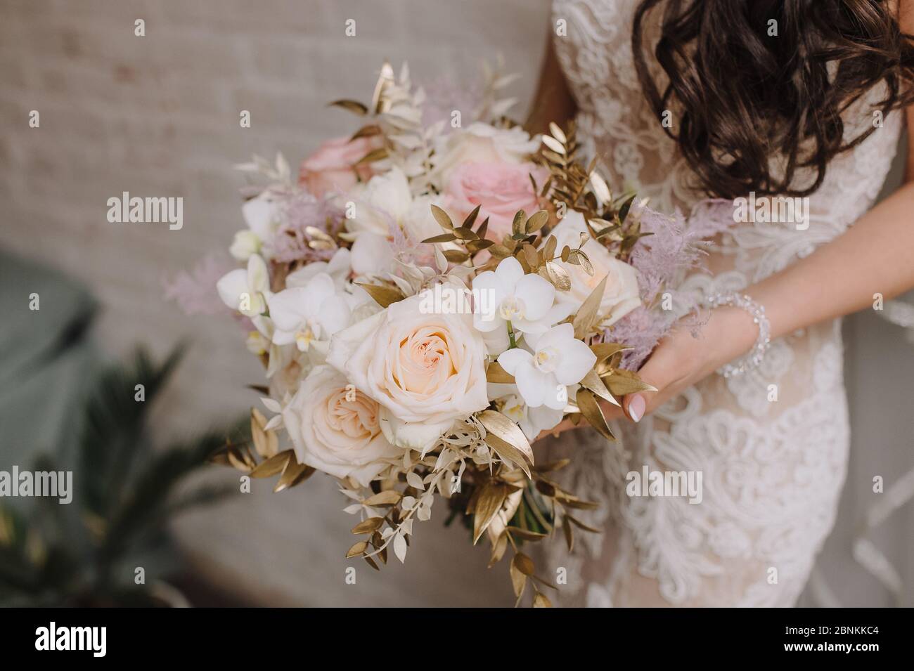 Nahaufnahme des Straußes einer Braut aus Pfirsich-Rosen, Nelken, goldenen Eukalyptusblättern. Die Braut in einem weißen Kleid mit langen Ärmeln hält einen Strauß in Stockfoto