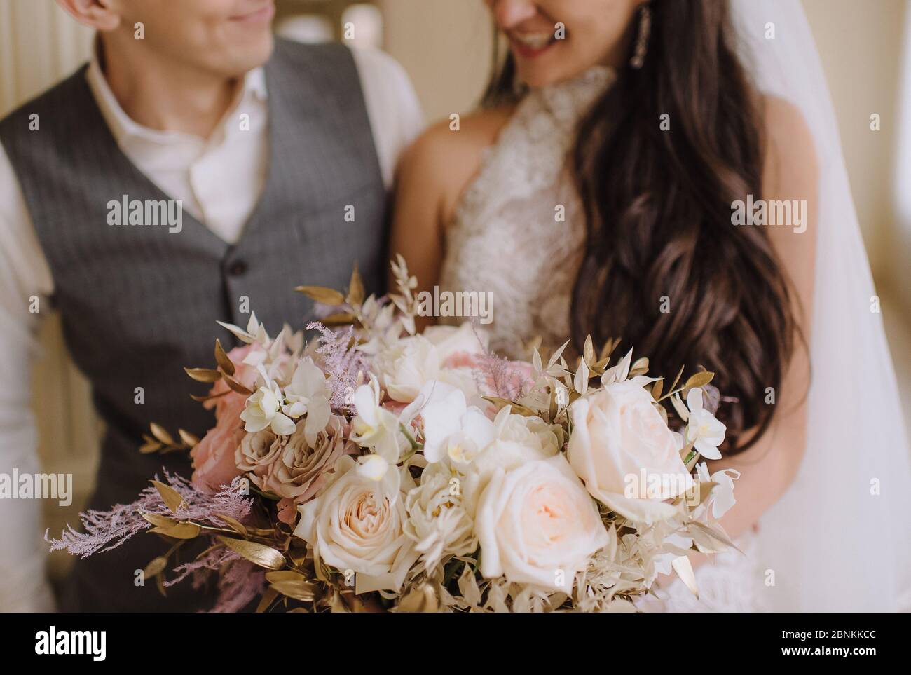 Nahaufnahme des Straußes einer Braut aus Pfirsich-Rosen, Nelken, goldenen Eukalyptusblättern. Die Braut in einem weißen Kleid mit langen Ärmeln hält einen Strauß in Stockfoto