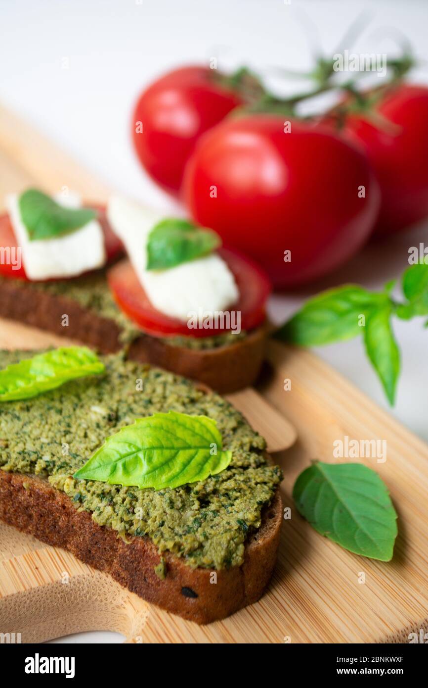 Traditionelle italienische Caprese Bruschetta: Sandwich Toast mit Basilikum Pesto Sauce, Mozzarella Käse und Tomaten auf dem Holzbrett von Basilikum l umgeben Stockfoto