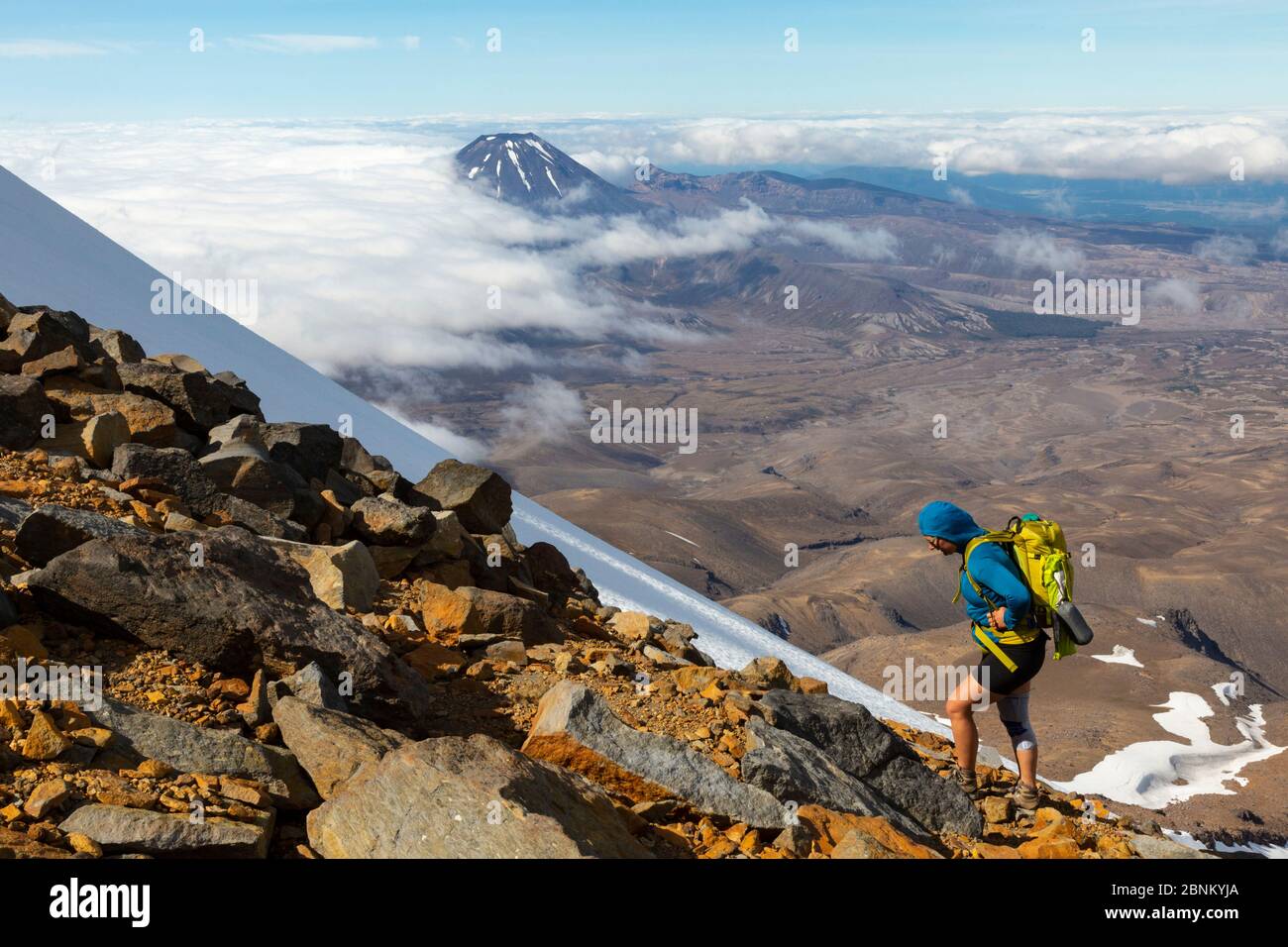Eine Kletterin steigt auf felsigem Gelände auf dem Mount Ruapehu mit Mount Ngauruhoe im Hintergrund, Tongariro National Park, Neuseeland Stockfoto