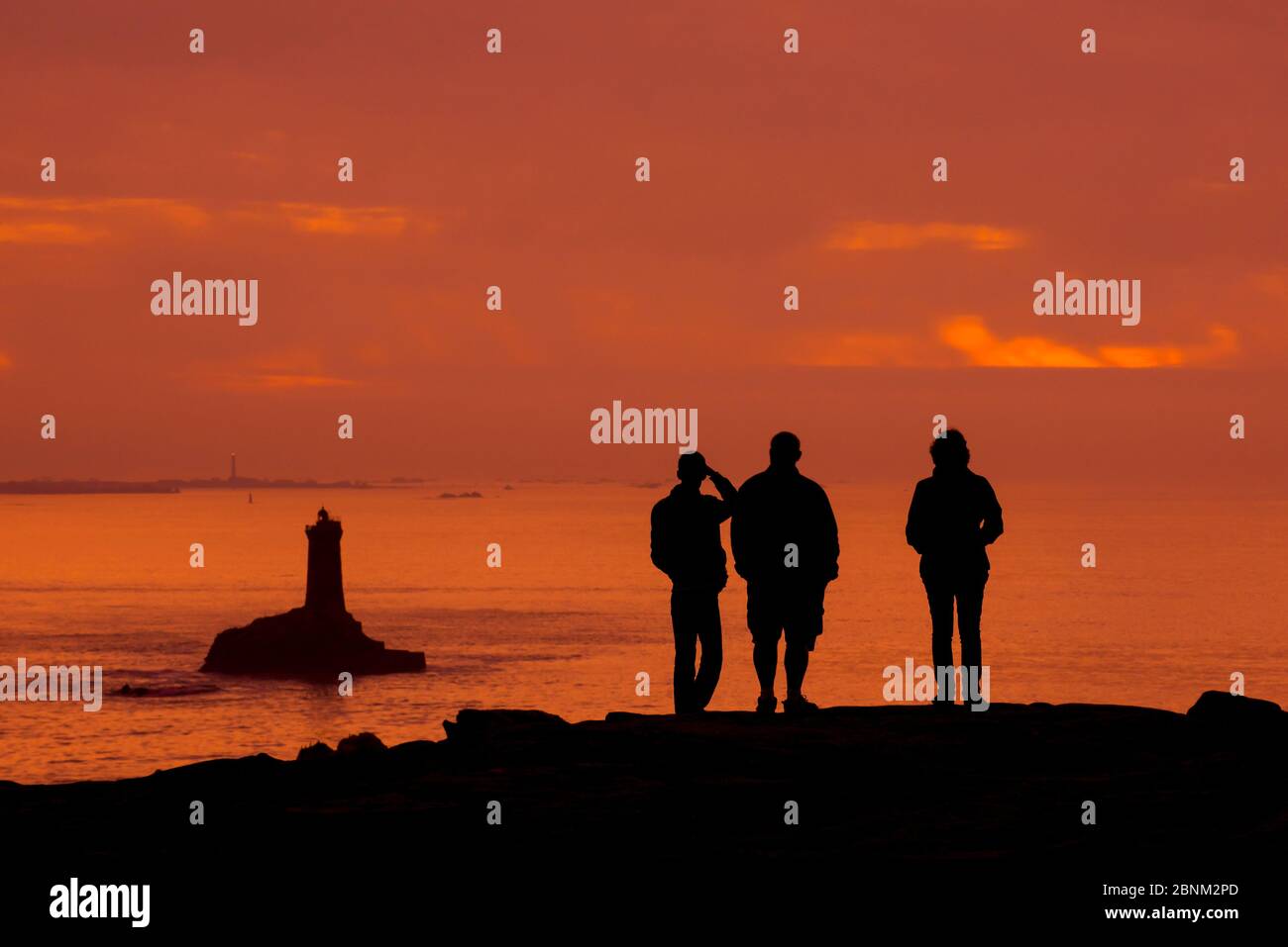 Touristen beobachten den Leuchtturm La Vieille in der Meerenge Raz de sein Silhouette gegen Sonnenuntergang an der Pointe du Raz, Plogoff, Finistere, Bretagne, F Stockfoto