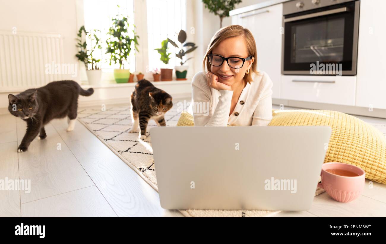 Freiberufliche Frau liegt im Wohnzimmer auf dem Teppich, Webinar ansehen. Hündin mit zwei Katzen im Gespräch durch Video-Chat mit ihrer Familie, die in Isolation du sind Stockfoto