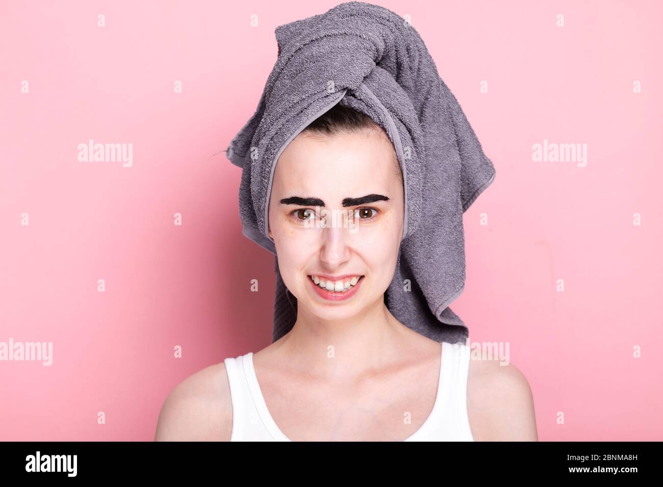 Junge Frau mit Handtuch auf dem Kopf malt ihre Augenbrauen auf sich. Etwas ging schief. Konzept Spa Tag zu Hause und in Quarantäne Stockfoto