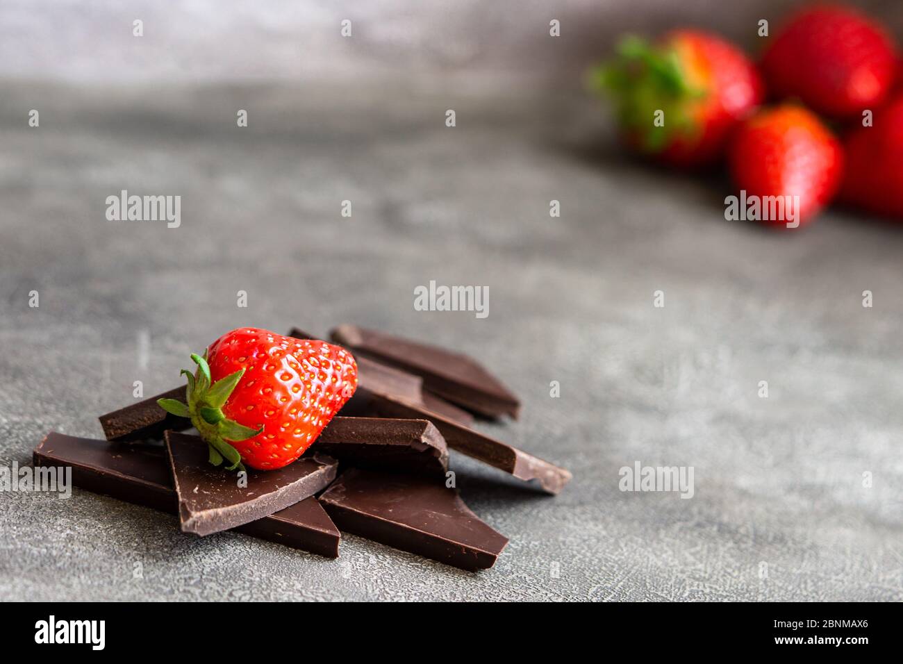 Stücke von dunkler Schokolade mit Erdbeere isoliert. Mehr Erdbeeren in der Ecke auf grauem Hintergrund. Kopierbereich, Nahaufnahme Stockfoto