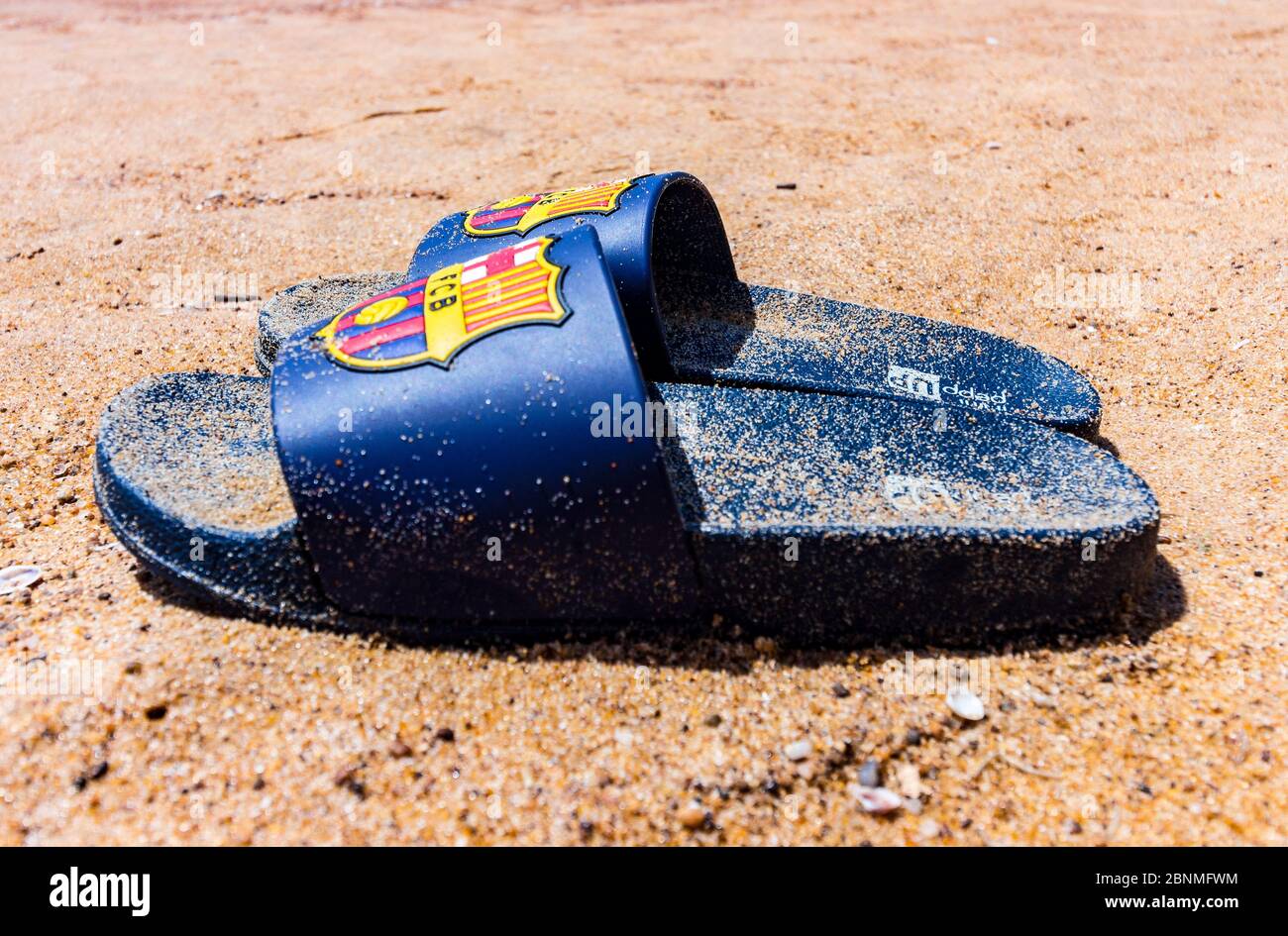Blaue Pantoffeln auf dem Sand des Candolim-Strandes in Nord-Goa, Goa, Indien mit einem Fußballverein namens Barcelona Logo darauf. Sandstrand in Goa. Stockfoto