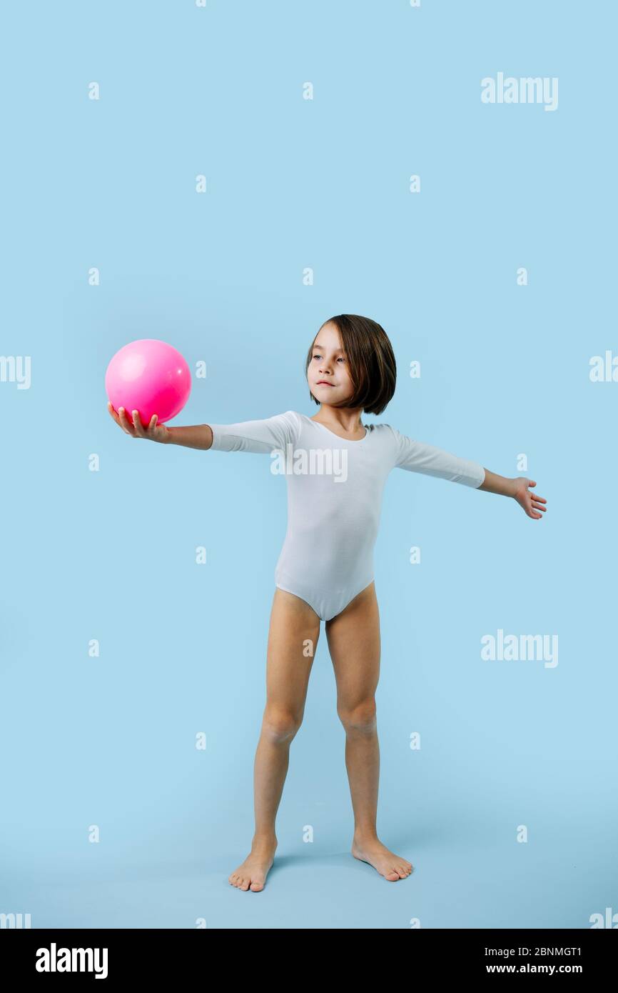 Kleines Mädchen in einem weißen Trikot mit Gymnastikball über blau Stockfoto