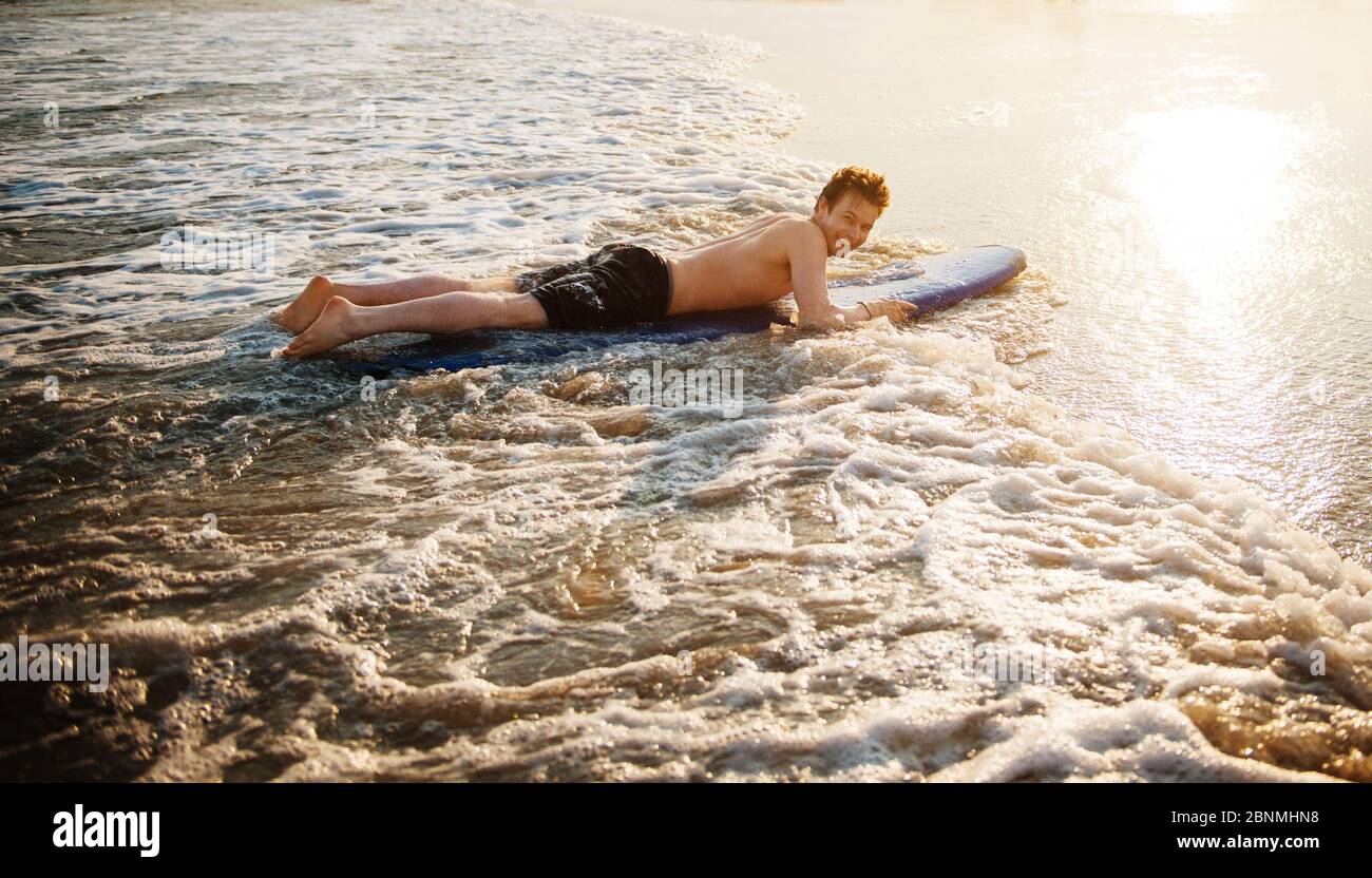 Junger Mann surft am Strand Stockfoto
