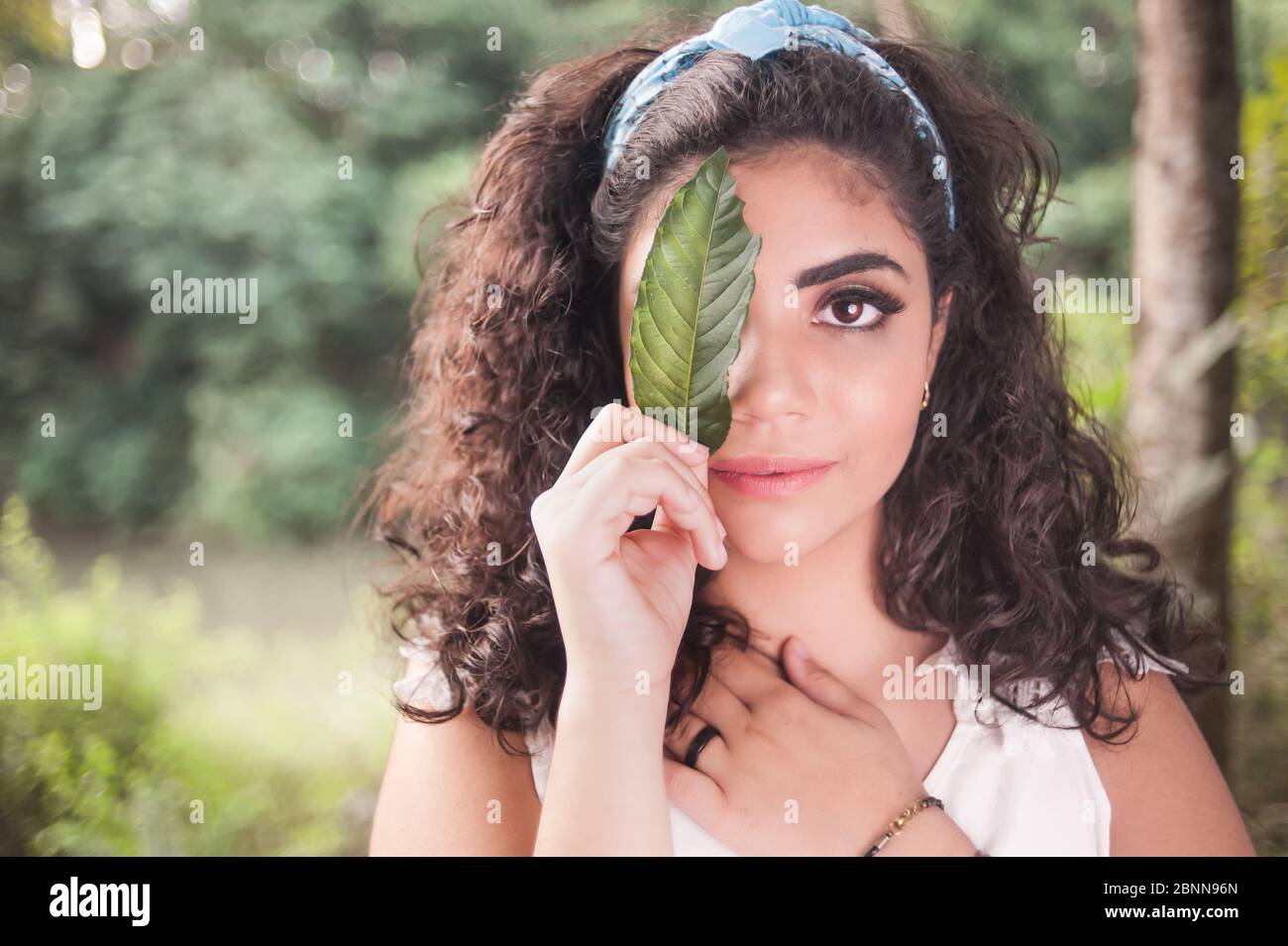 Schönes Mädchen aus nächster Nähe Hoding ein Blatt auf ihr Gesicht. Sie hat einen friedlichen Ausdruck Stockfoto