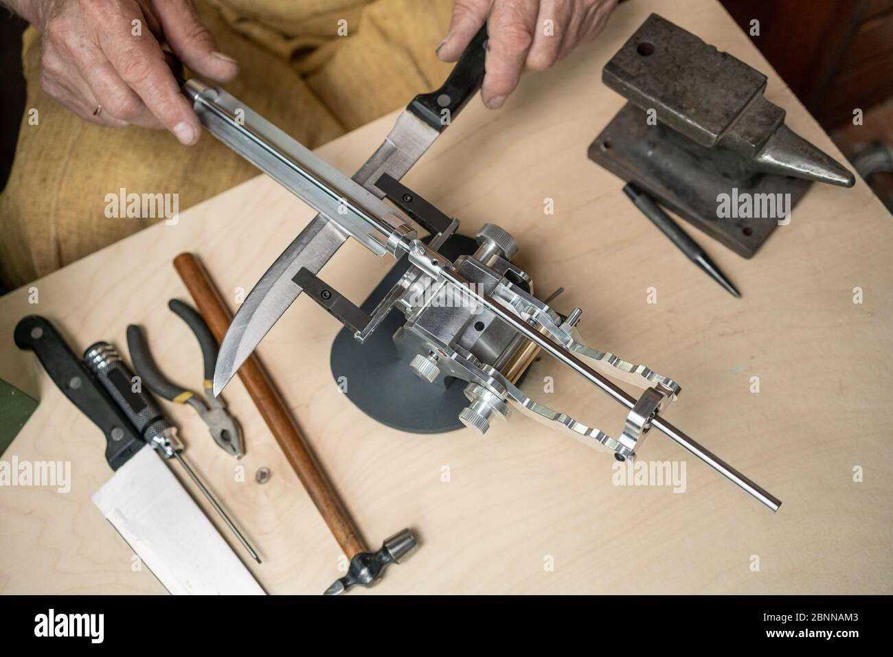 Herstellung eines Messers. Meister schärft eine Klinge auf der Maschine Nahaufnahme im Studio Stockfoto