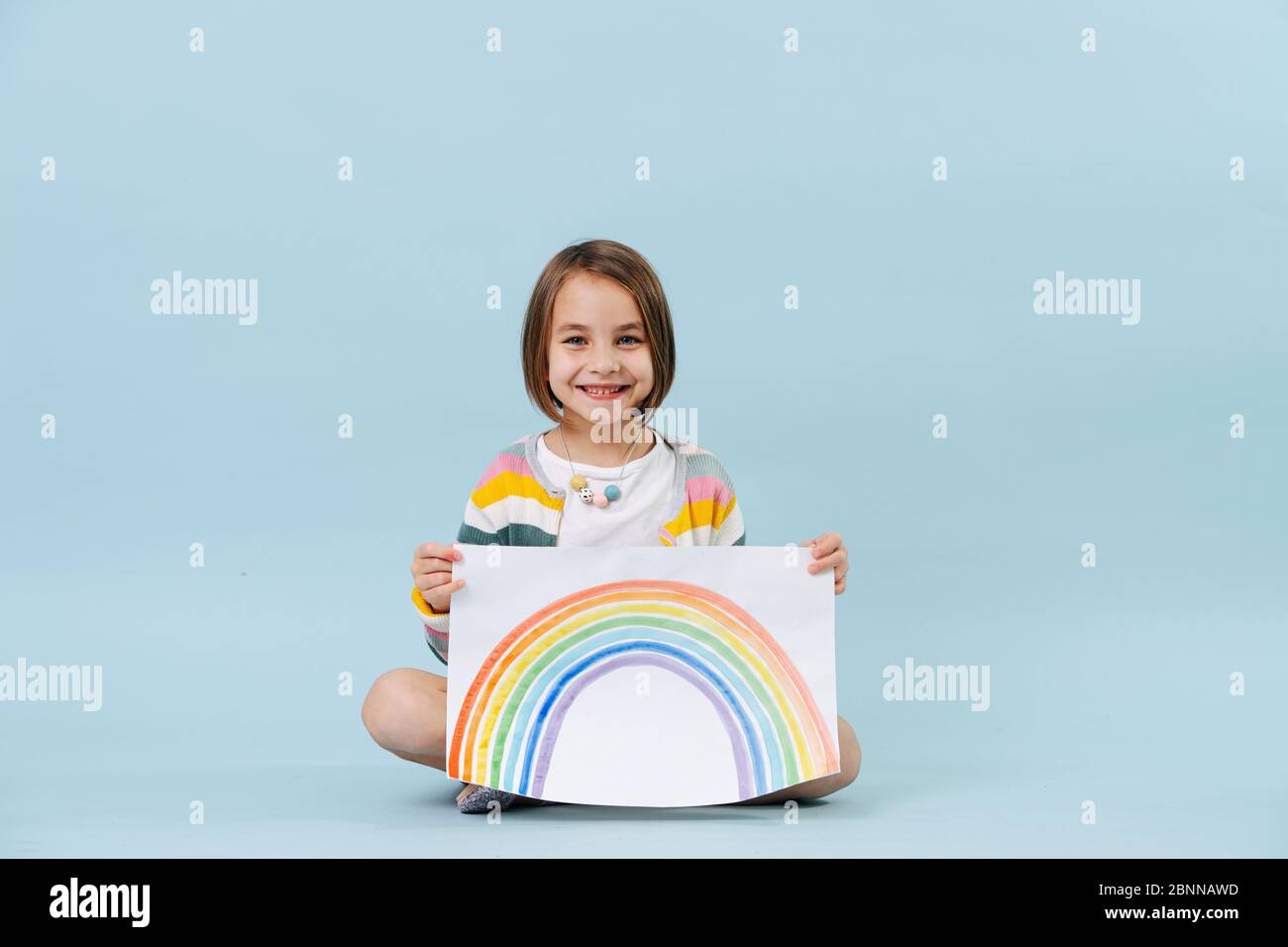 Fröhliches kleines Mädchen zeigt einen Regenbogen, den sie gerade gemalt hat Stockfoto