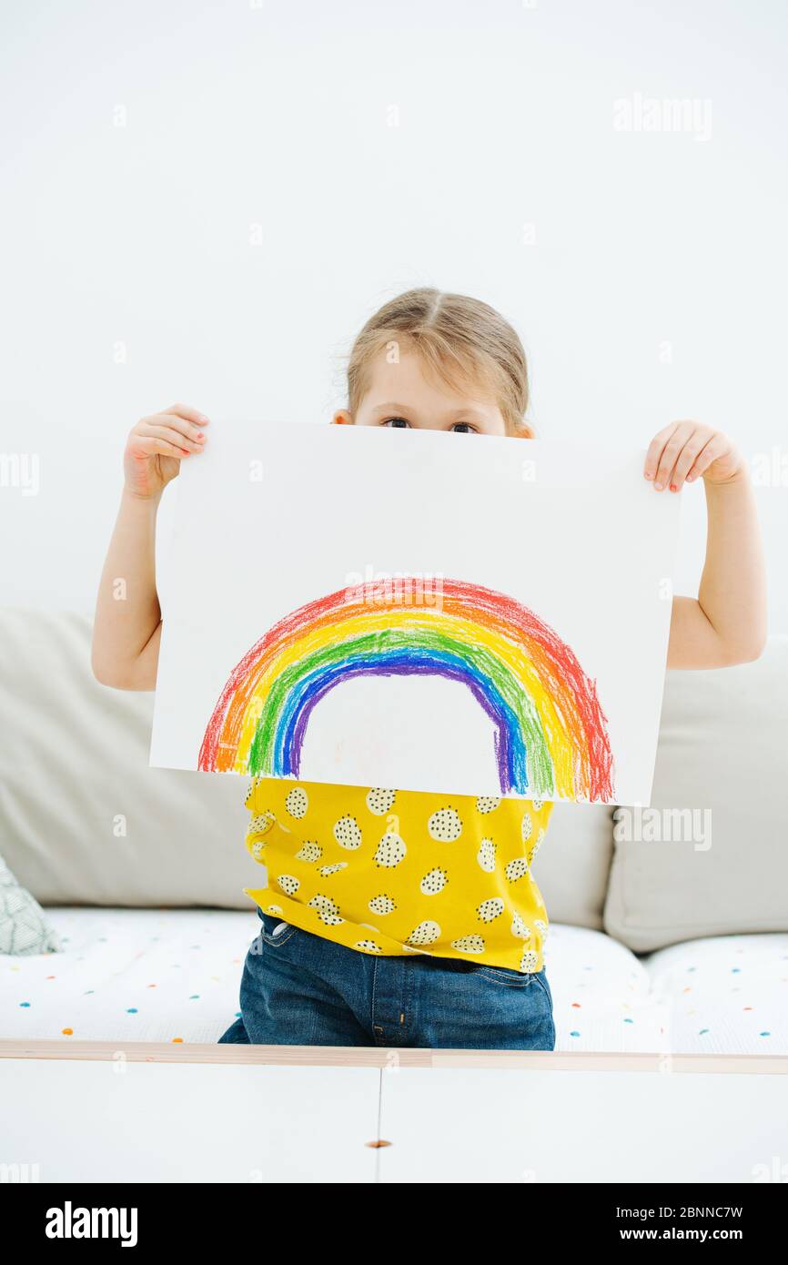 Kleines Mädchen, das ein Blatt Papier mit einem Regenbogen hält, den sie gerade gemalt hat Stockfoto