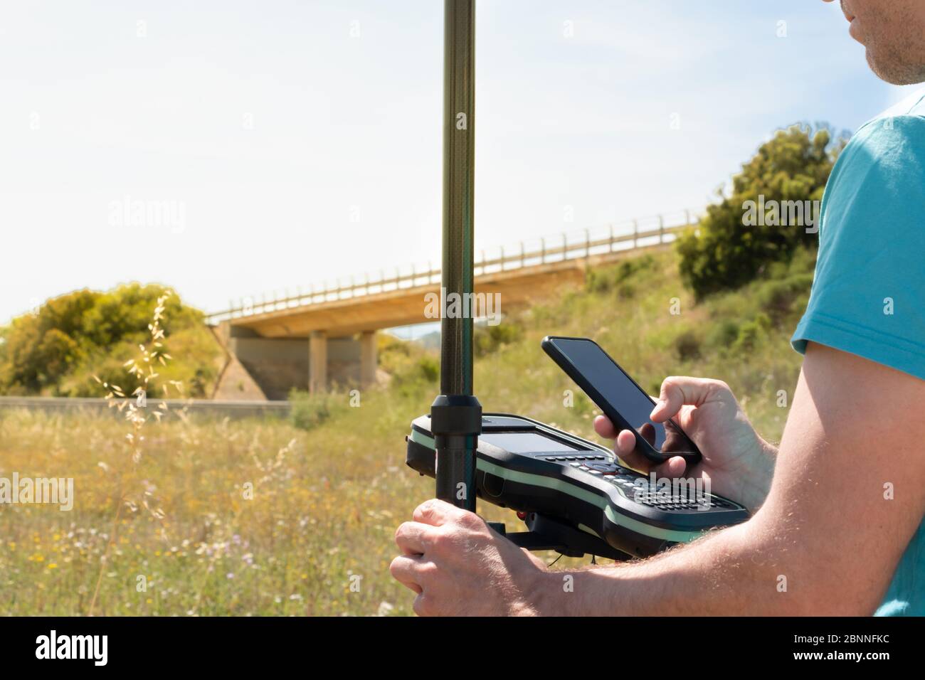 Landvermesser arbeitet mit einem GPS-Instrument, prüft Daten online mit seinem Smartphone. Außendienst Stockfoto