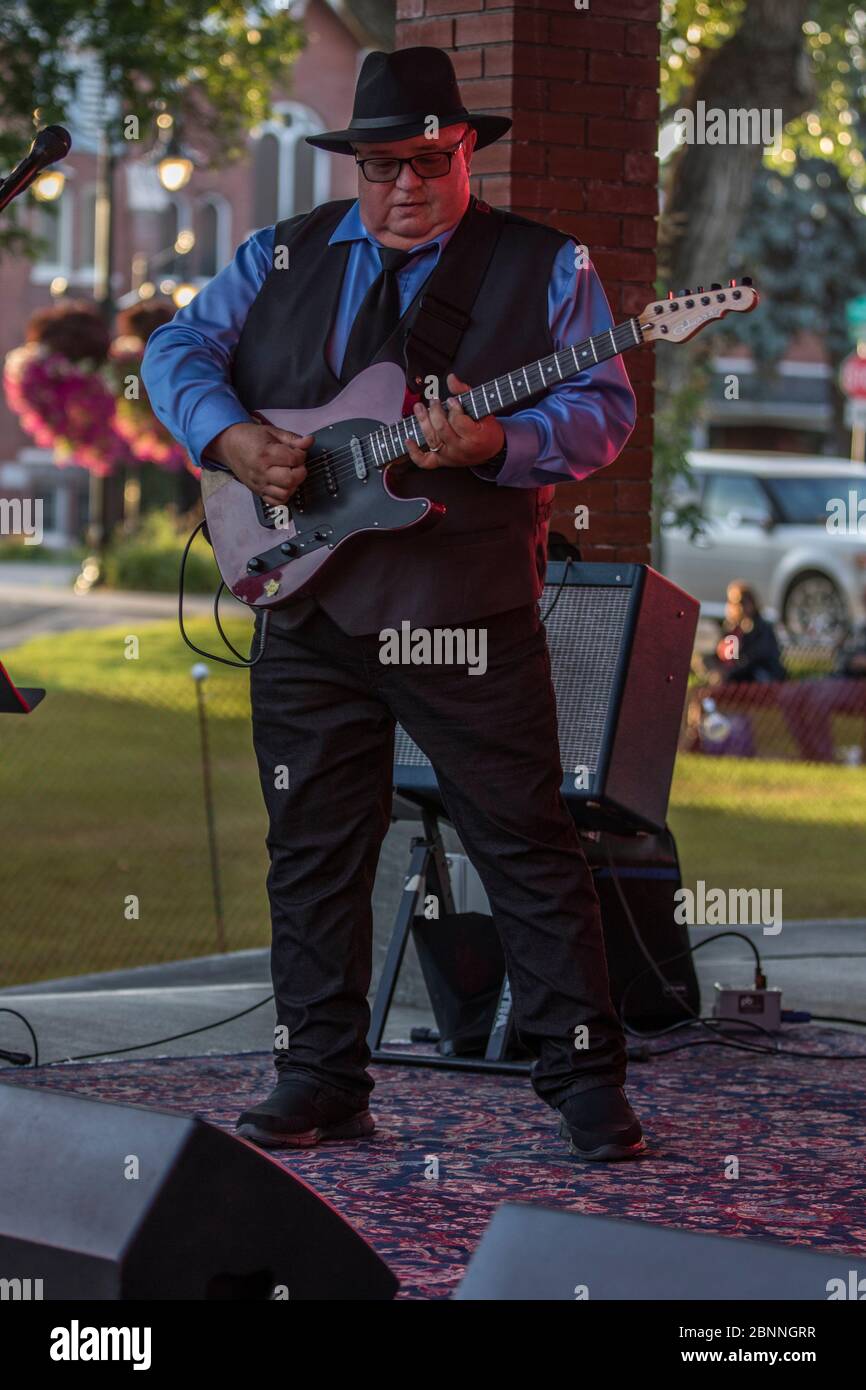 Senior Male Sänger und Lead-Gitarrist, in Outdoor-Konzert, trägt Fedora Hut und Sonnenbrille. Stockfoto