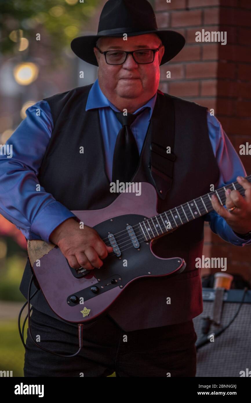 Senior Male Sänger und Lead-Gitarrist, in Outdoor-Konzert, trägt Fedora Hut und Sonnenbrille. Stockfoto