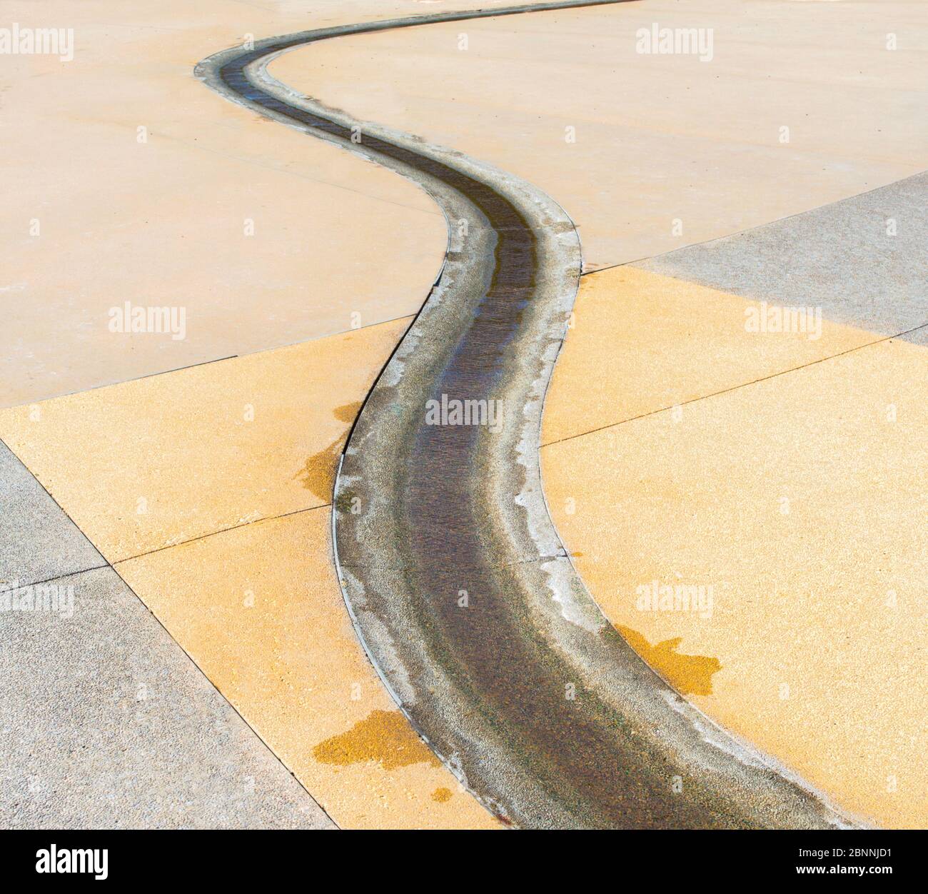 Ein kleiner Zement-Außenwasserstraße schlängelt sich durch einen leeren Bürgersteig mit Kopierraum Stockfoto