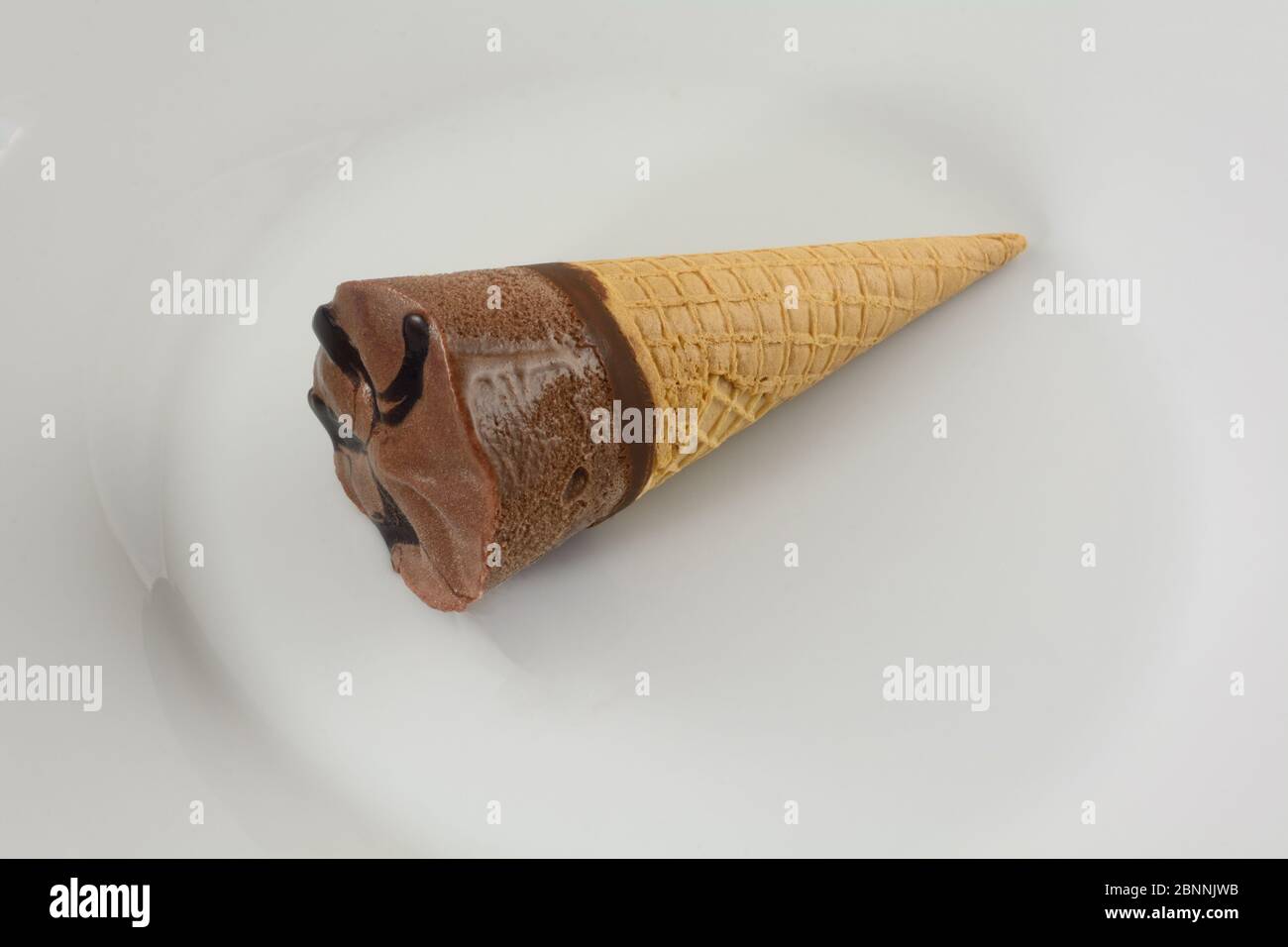 Schokoladeneis-Konus mit Fudge-Belag auf weißem Teller Stockfoto