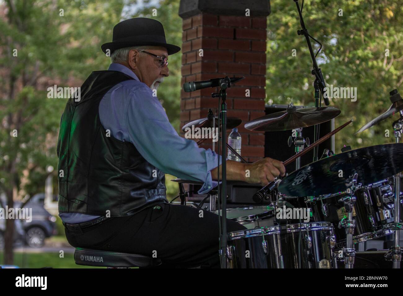 Senior männlich, scharf gekleidet, mit Fedora Hut, Schlagzeug spielen, in Rockband bei Outoor Konzert. Stockfoto