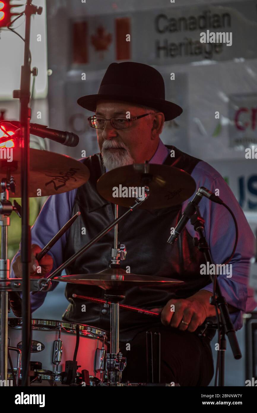 Senior männlich, scharf gekleidet, mit Fedora Hut, Schlagzeug spielen, in Rockband bei Outoor Konzert. Stockfoto