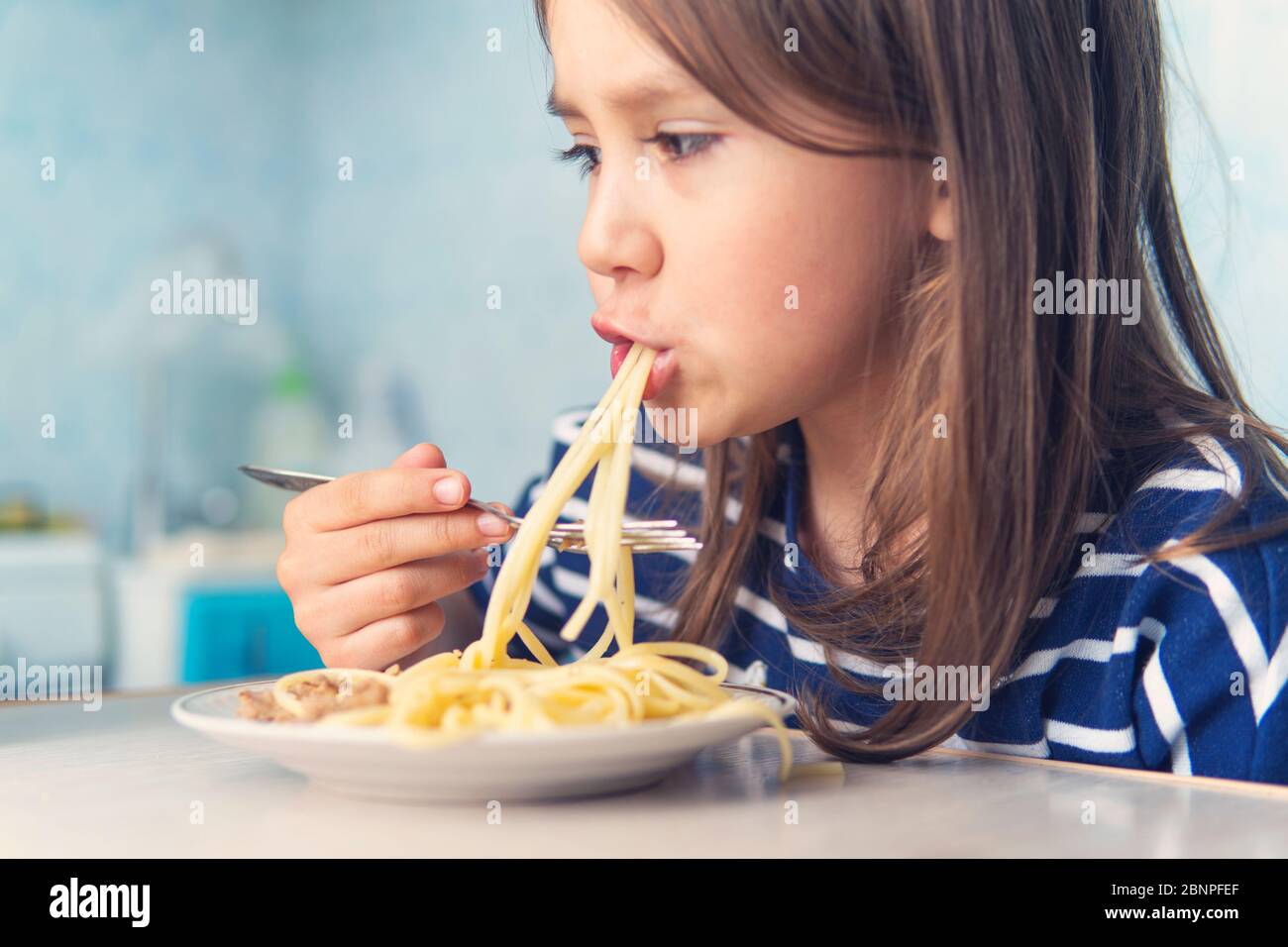 Das Kind isst eifrig leckere Pasta in der Küche Stockfoto