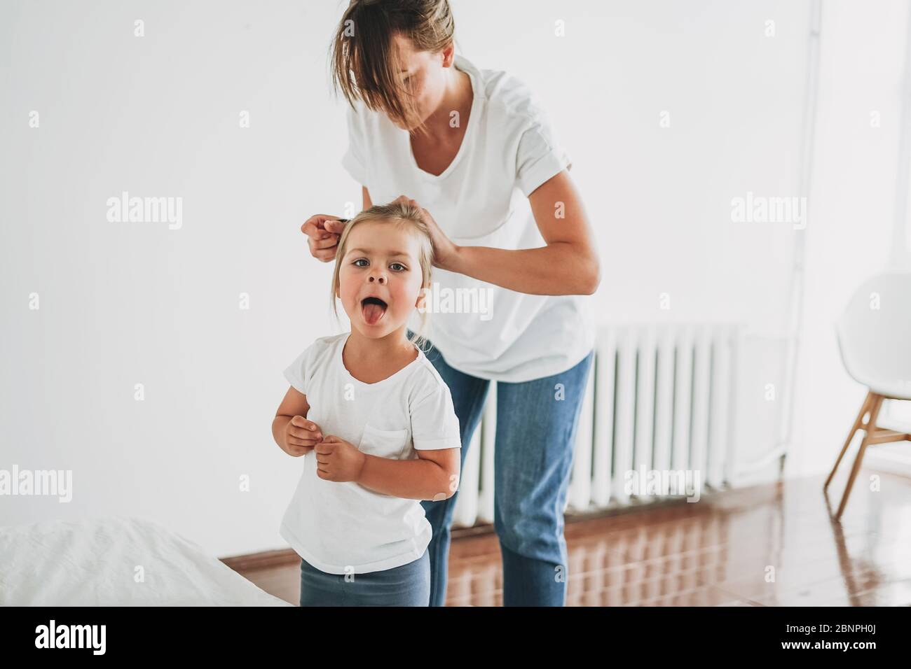 Lustige Moment des realen Lebens, wenn junge Mutter zu ihrer Tochter Kleinkind Mädchen Pony Schwanz in hellen Raum tun Stockfoto