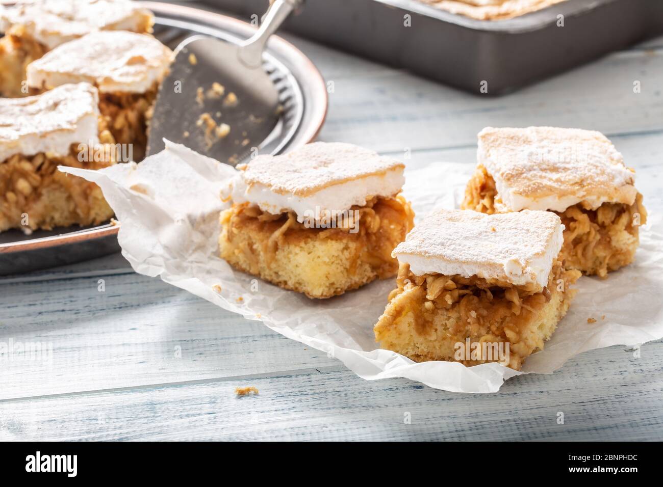 Drei Würfel Apfelkuchen mit einem gewissten wgg Weiß, das auf einer Serviette mit mehr Kuchen im Rücken umtoppen. Stockfoto
