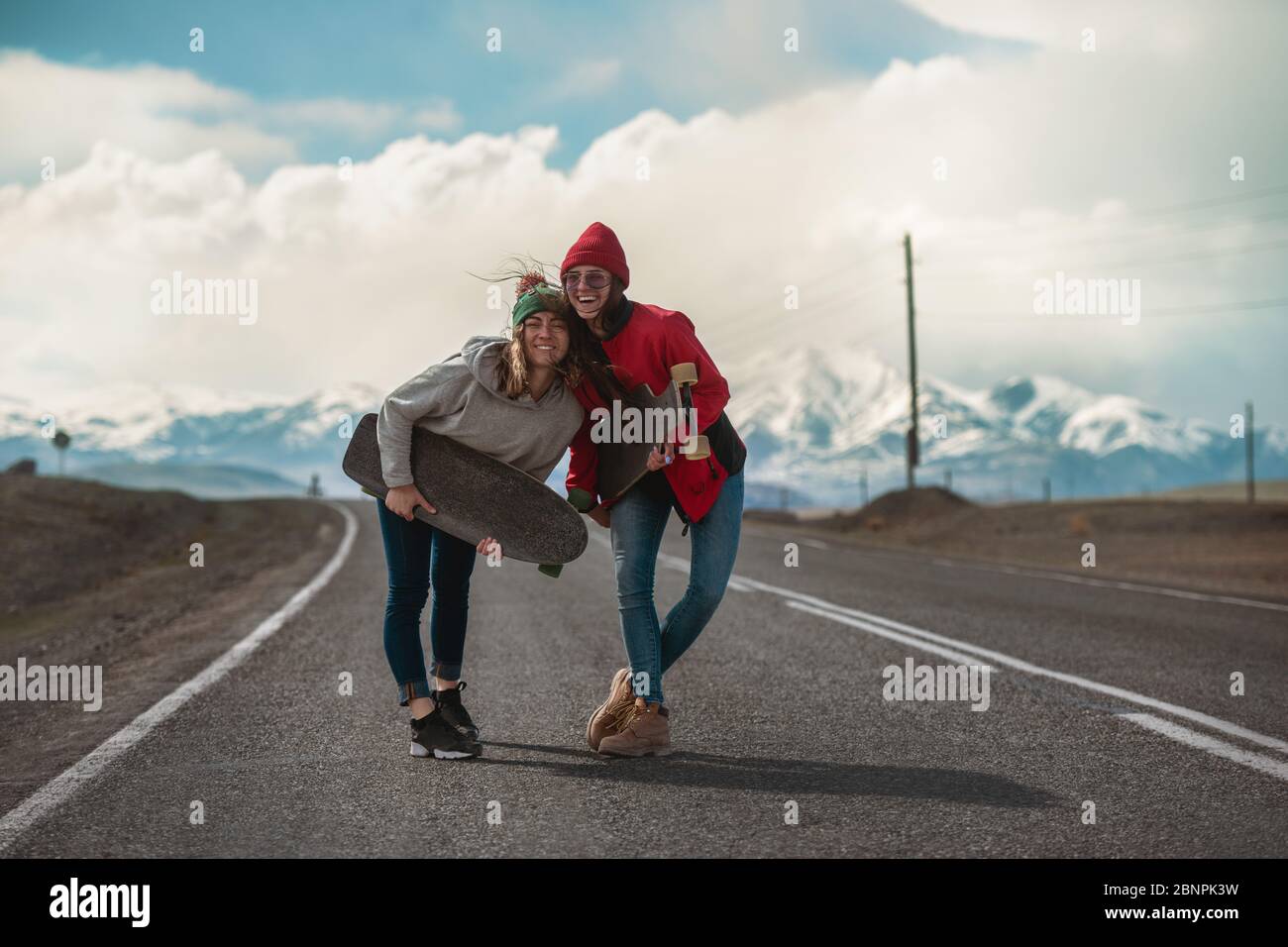 Zwei glückliche junge Mädchen stehen mit Longboards an der Bergstraße und haben Spaß Stockfoto