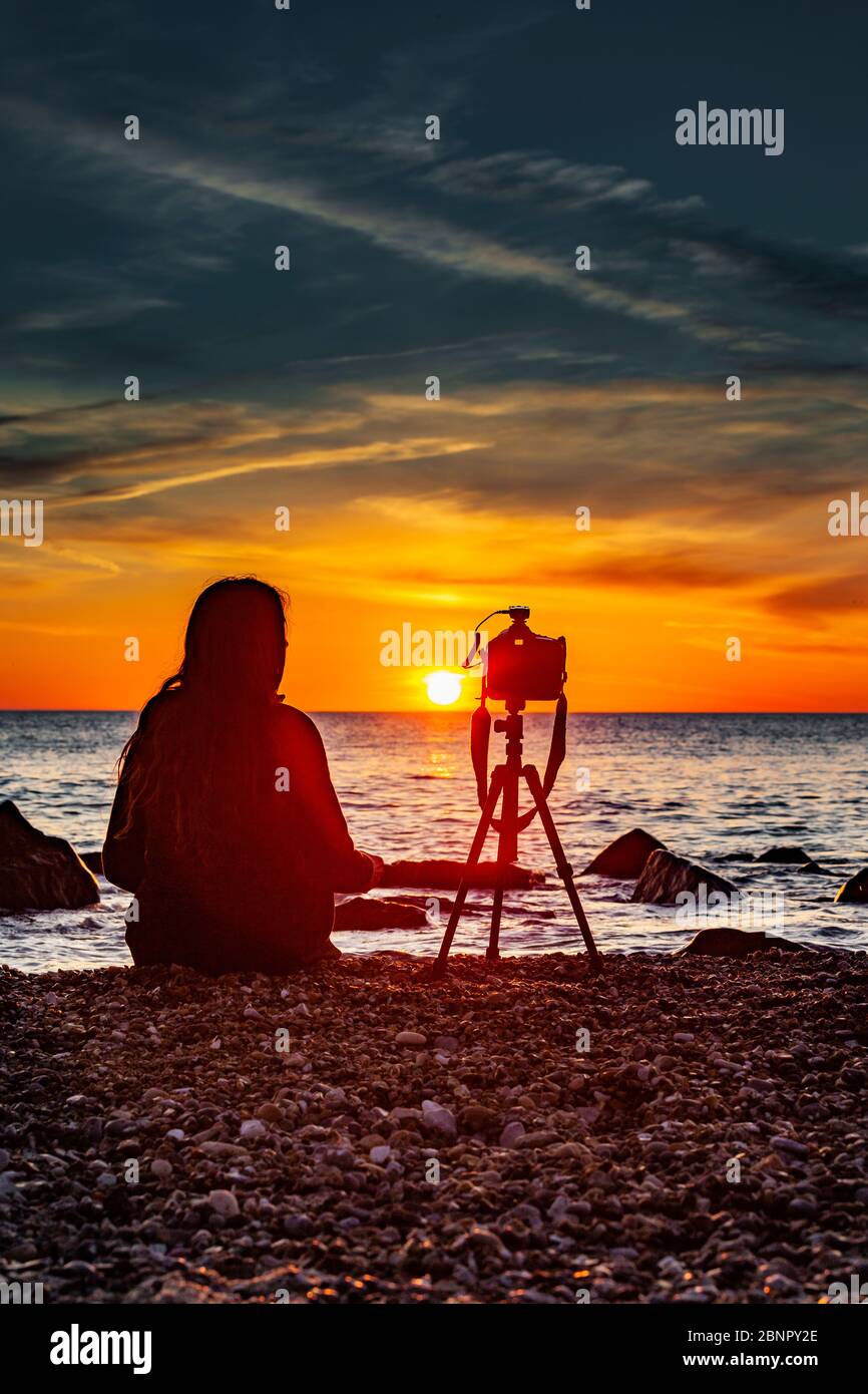 Weibliche Silhouette mit Kamerastativ bei Sonnenuntergang am Meer Stockfoto