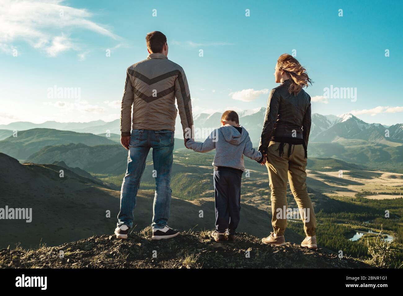 Familie von Vater, Mutter und Kind steht in den Bergen und schaut auf Sonnenuntergang Stockfoto