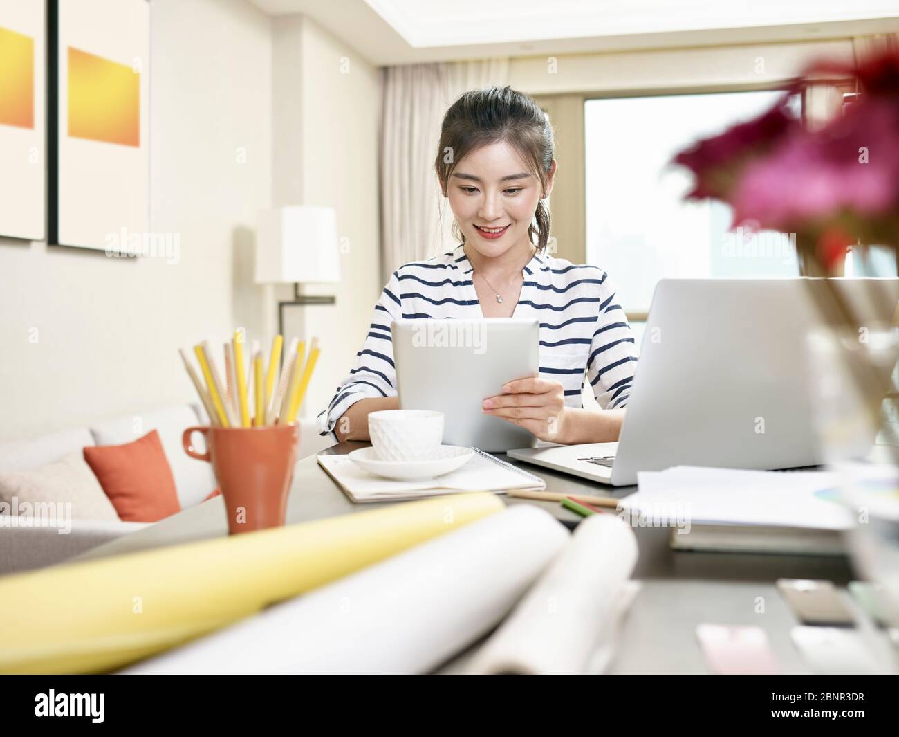 Junge asiatische Geschäftsfrau arbeitet zu Hause mit Laptop-Computer und digitalen Tablet (Kunstwerk im Hintergrund digital verändert) Stockfoto
