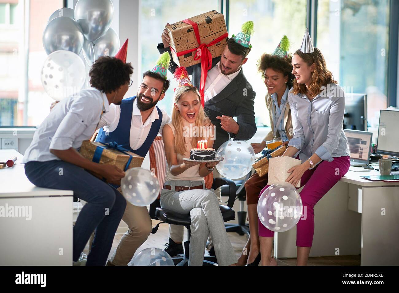 Überraschung Geburtstagsfeier im Büro. Glückliche Mitarbeiter feiern mit Ballonen, Geschenken und Kuchen. Thema der Büroparty. Stockfoto