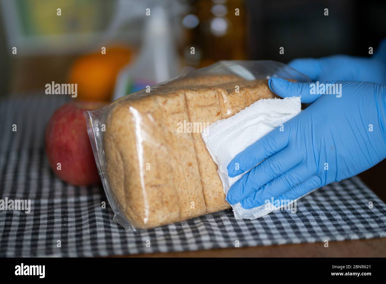 Eine Frau, die Handschuhe trägt, wischt während der COVID-19 Pandemie 2020 die Umverpackung eines Brotes ab Stockfoto