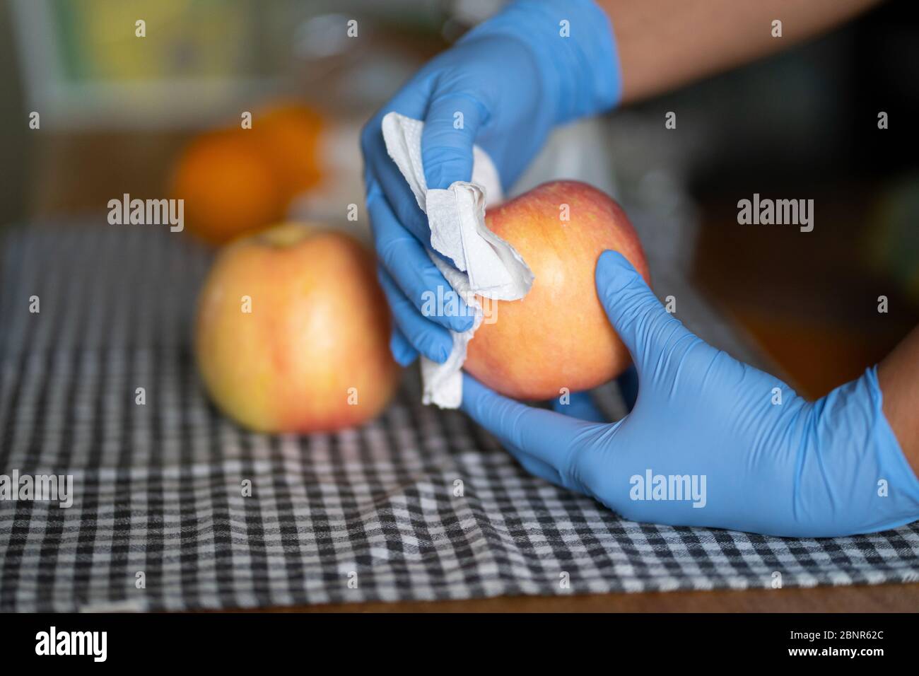 Eine Frau, die Handschuhe trägt, schneidet während der COVID-19 Pandemie 202 einen Apfel mit einem Wischtuch Stockfoto