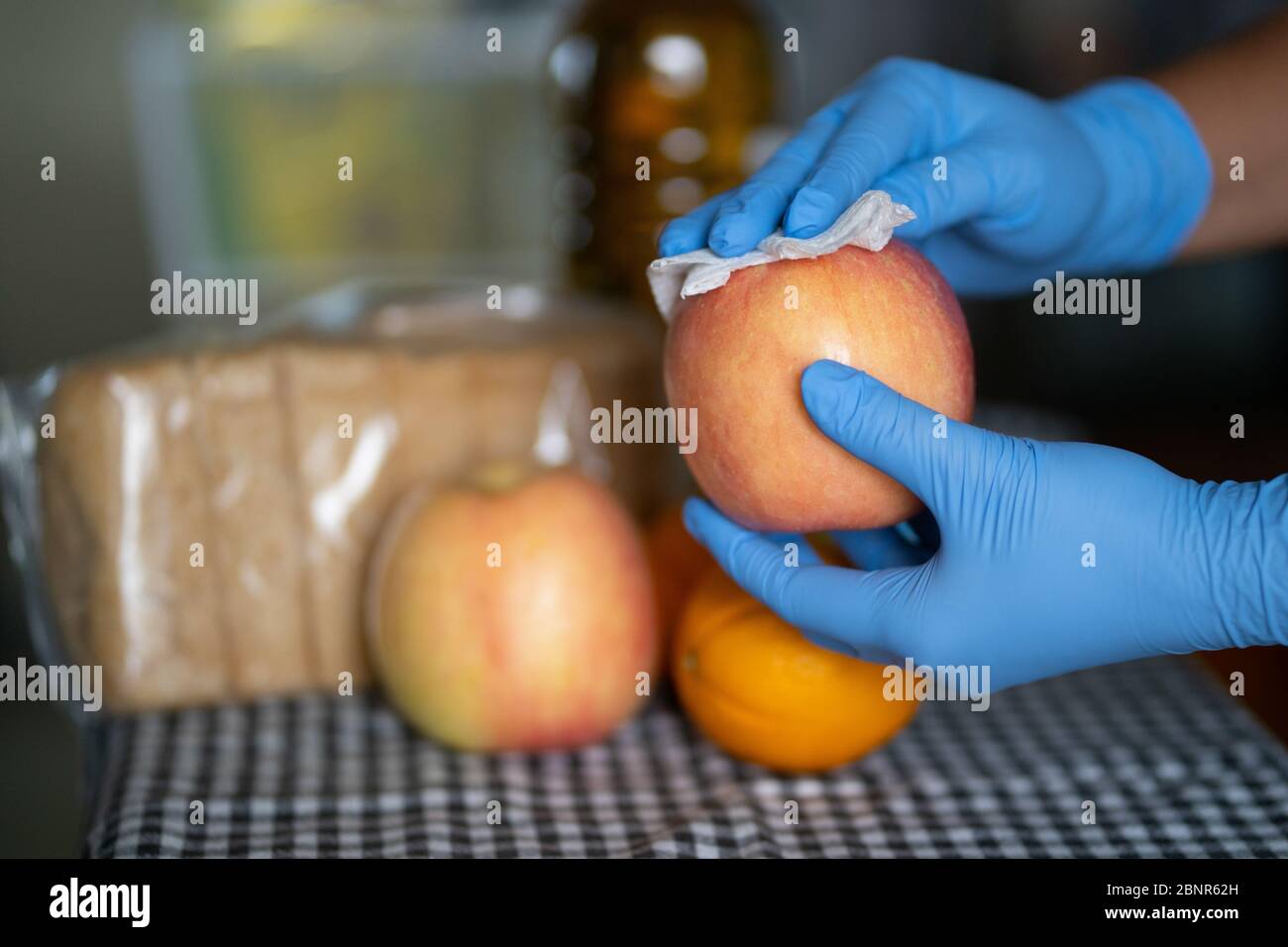 Eine Frau, die Handschuhe trägt, schneidet während der COVID-19 Pandemie 2020 einen Apfel mit einem Wischtuch Stockfoto