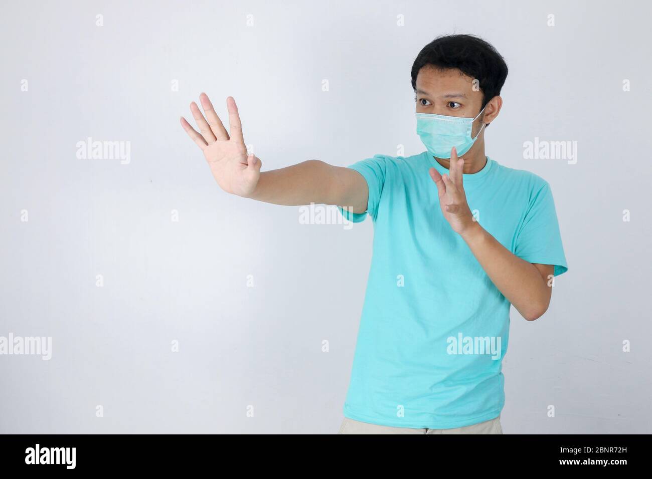 Junge asiatische Mann tragen hygienische Maske ist erschrocken oder Panik mit gesturing Stop Hand. Angst vor Coronavirus-Infektion oder Atemwegserkrankungen wie f Stockfoto