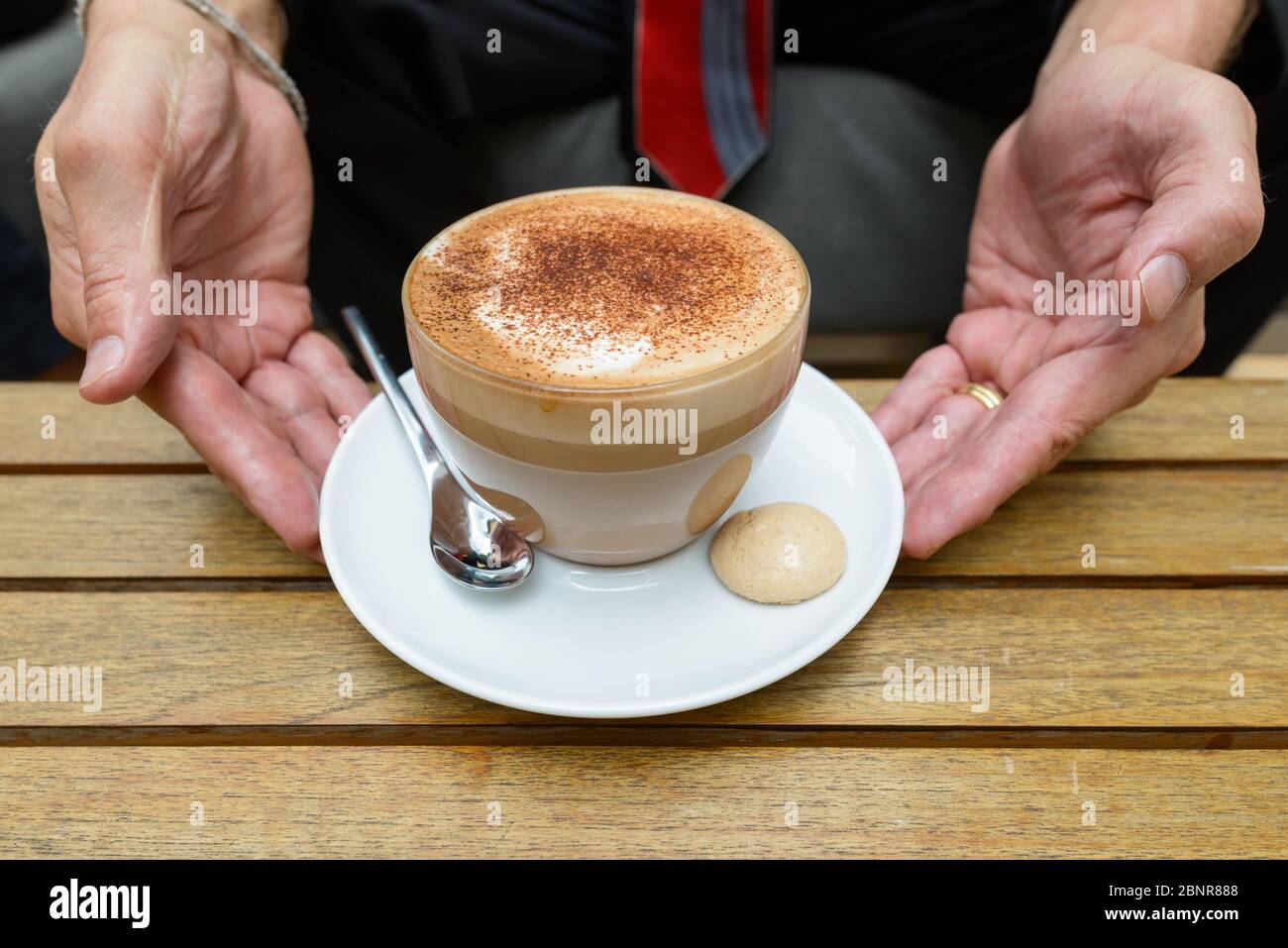 Geschäftsmann hält Tasse Cappuccino Kaffee mit Schokolade Streusel auf Schaum und Keks auf der Seite Stockfoto