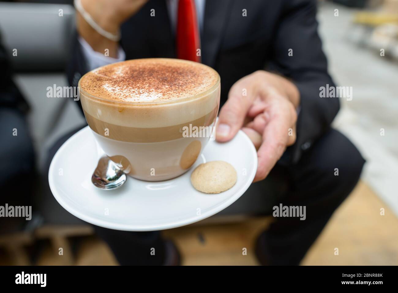 Geschäftsmann hält Tasse Cappuccino Kaffee mit Schokolade Streusel auf Schaum und Keks auf der Seite Stockfoto