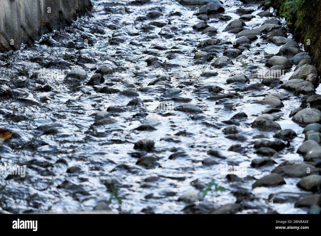 Wasser fließt durch einen Wasserweg mit runden Steinen auf dem Grund des Flusses gelegt Stockfoto